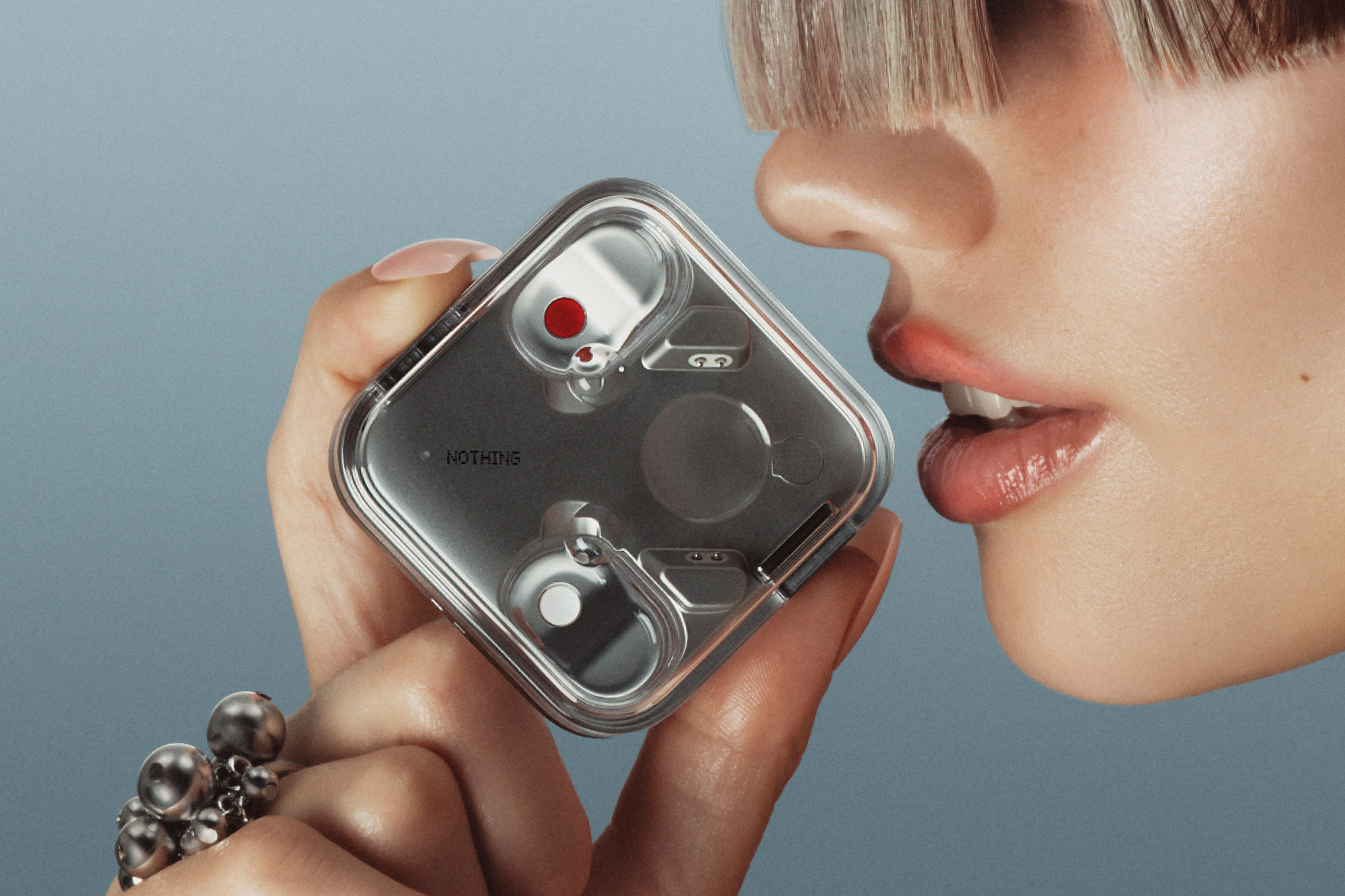 A woman holding the Nothing Ear 3 case close to her mouth to talk to it — Nothing recommends up to six inches.