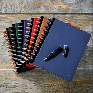 Several different colored overlapping notebooks with an open pen on top