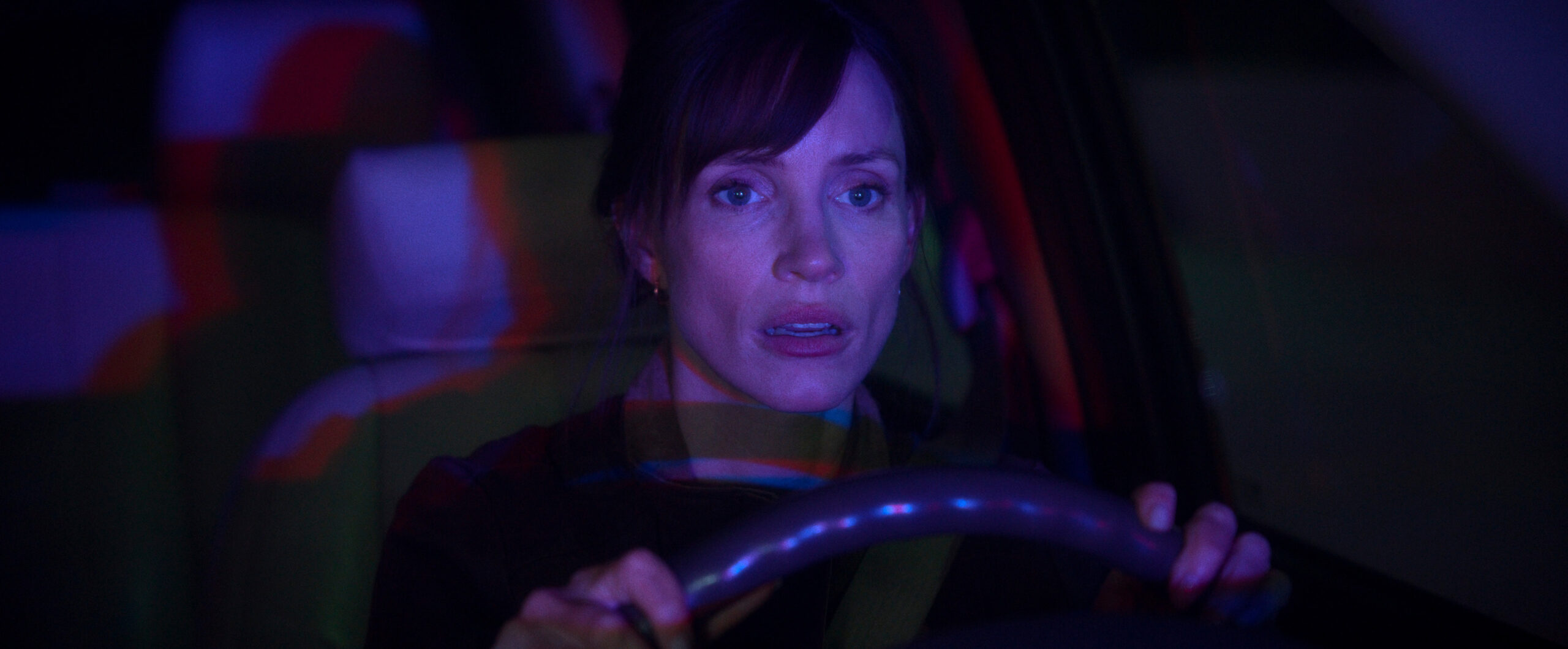 A woman sitting in the driver’s seat of a car with a look of shock on her face.