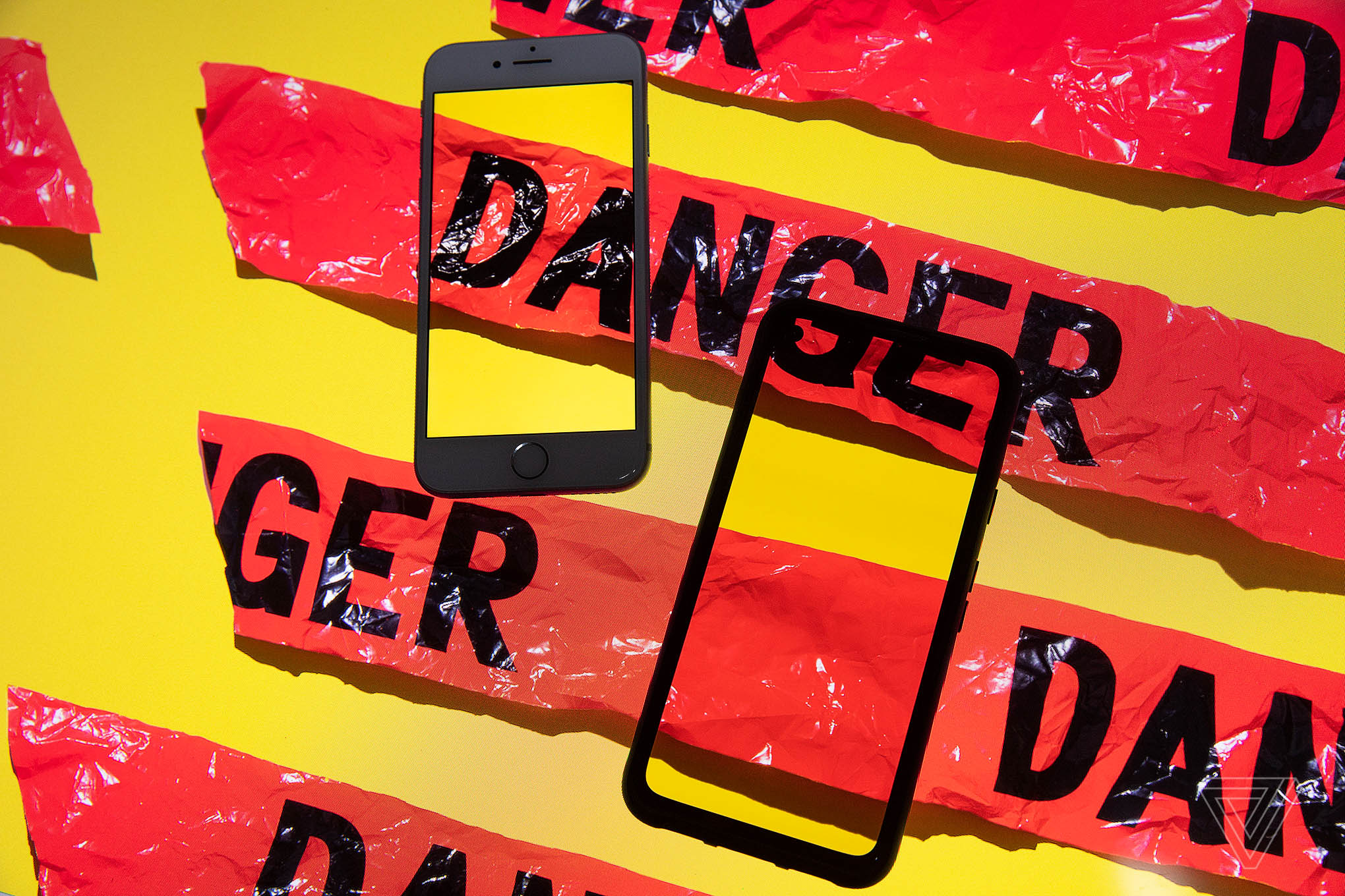 Smartphones sit on top of a surface with red tape reading “DANGER.” Where one strip intersects the phone, it continues inside the phone’s screen.