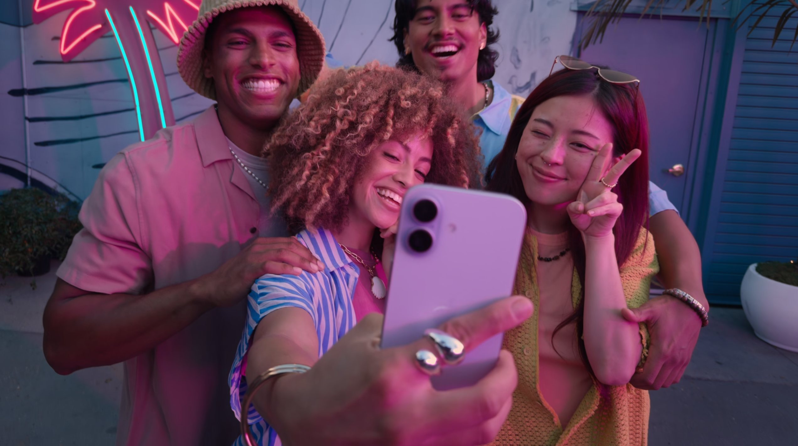 A group of people smiling for a selfie while the center-most person holds the iPhone 17.
