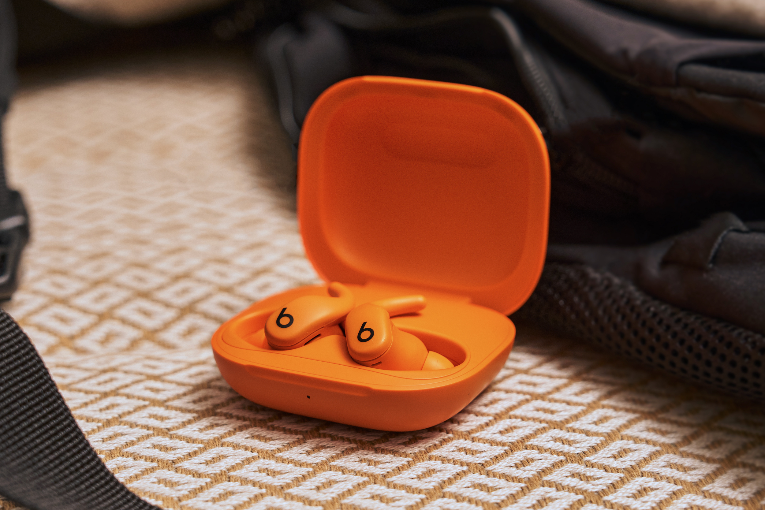 A photo of the spark orange version of the Beats Powerbeats Fit wireless earbuds.