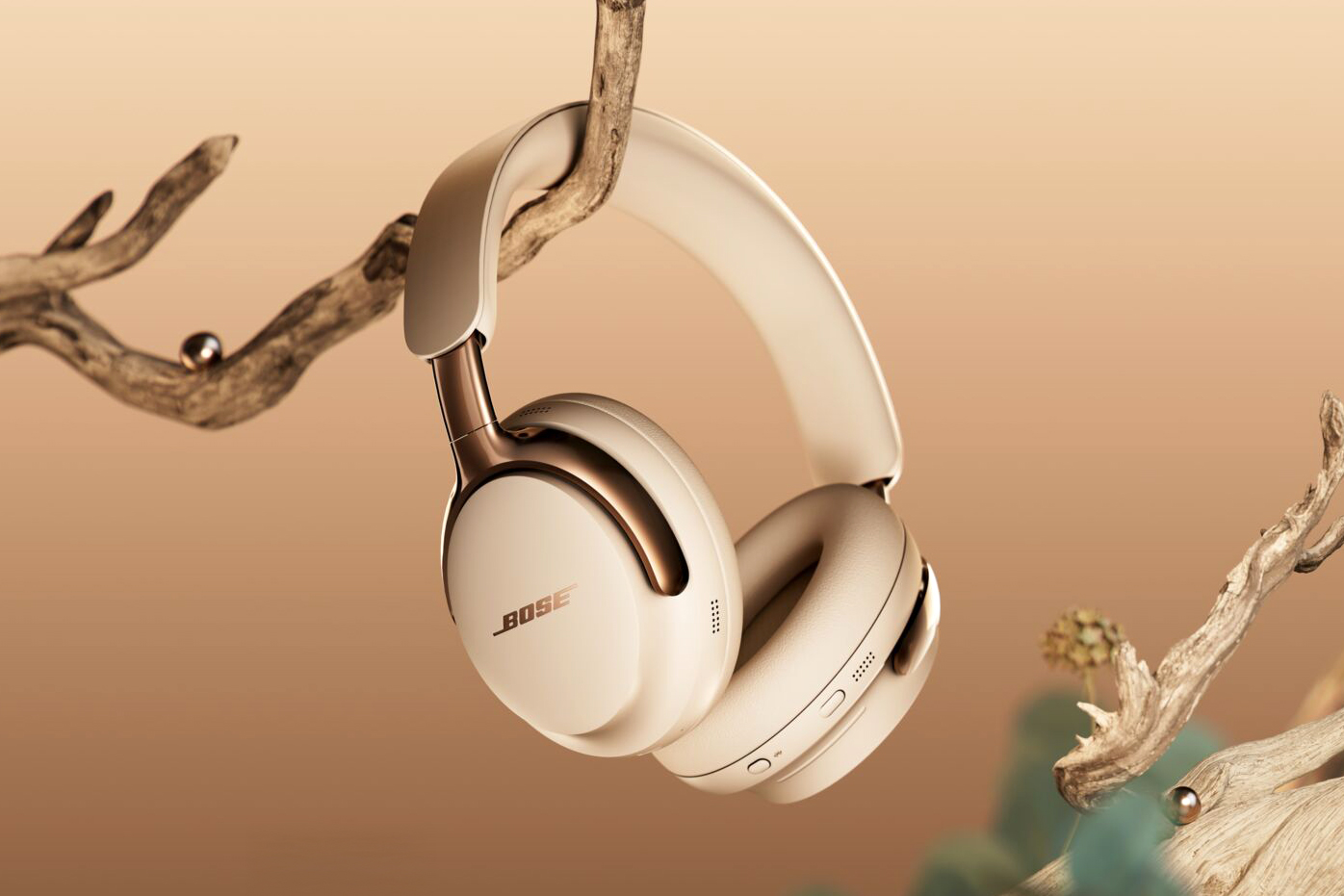 A pair of Bose’s new QuietComfort Ultra wireless headphones hanging on a tree branch.