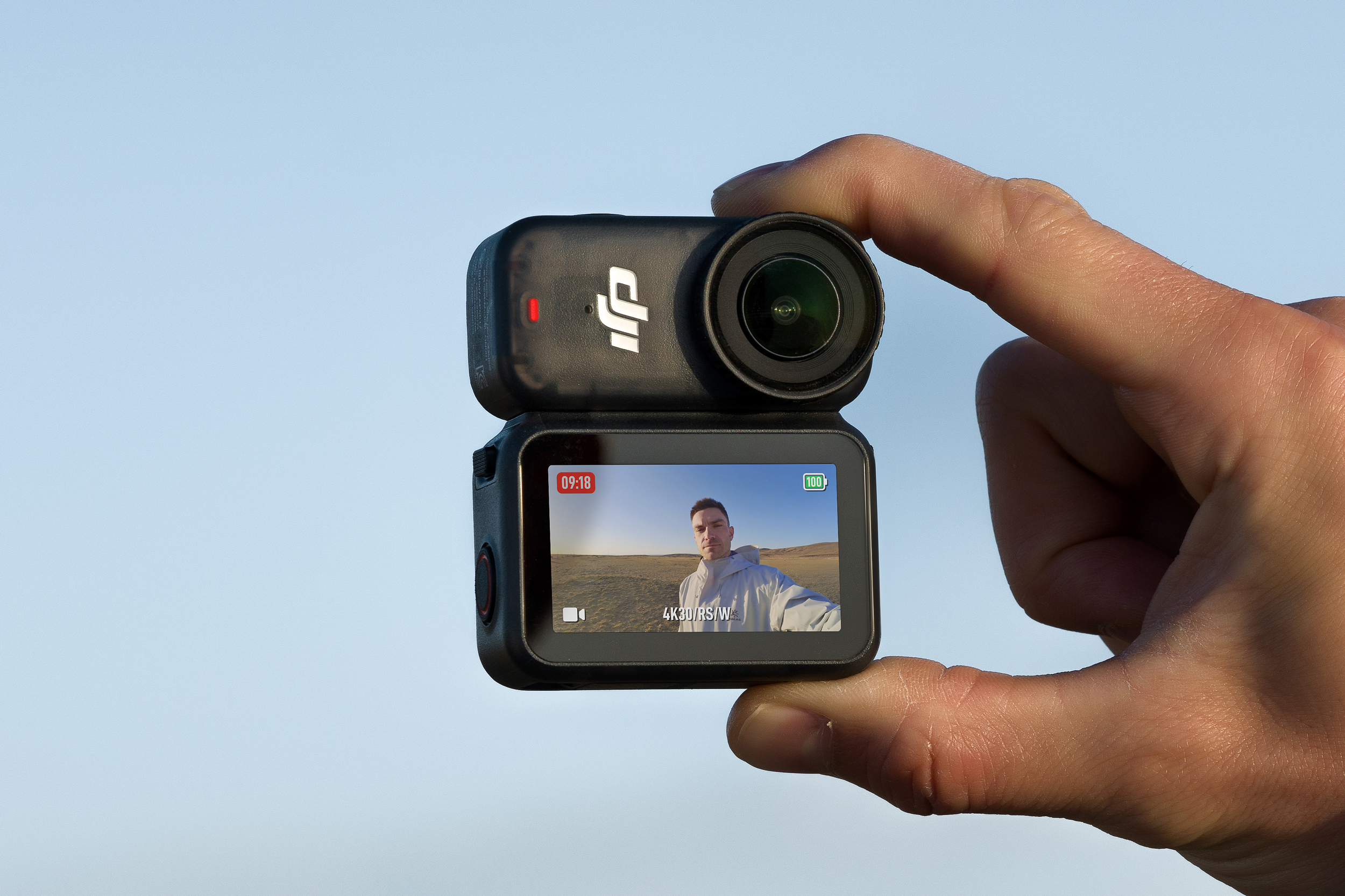 A person holds the DJI Osmo Nano action camera attached to its dock accessory between two fingers.
