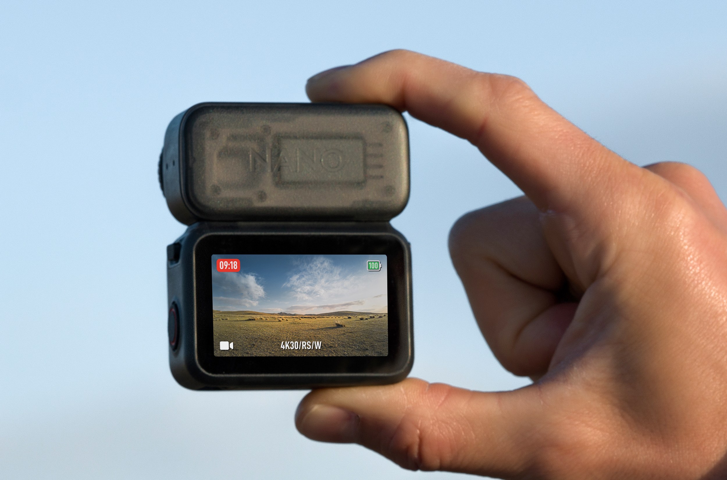 A person holds the DJI Osmo Nano camera attached to its touchscreen dock between two fingers.
