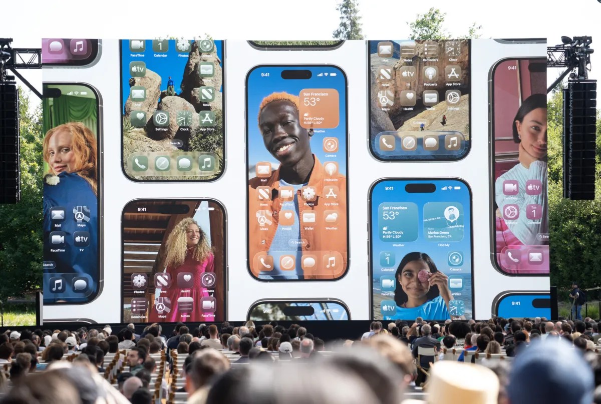 A photo of people looking at a screen showing iPhones with Apple’s iOS 26 update.