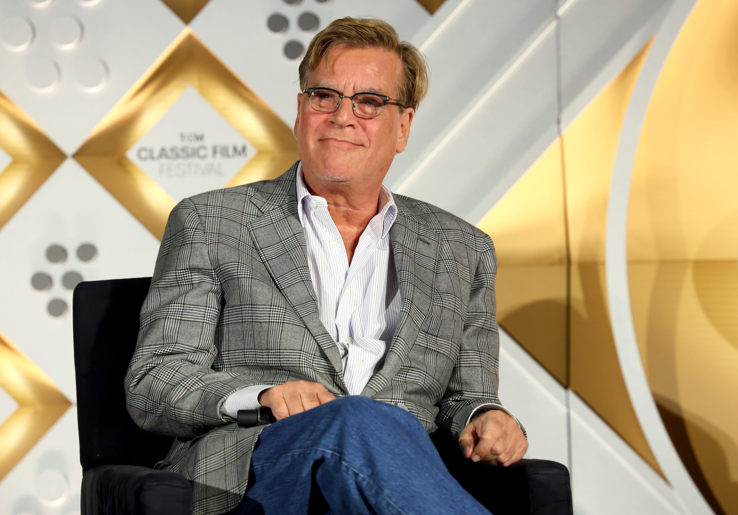 Aaron Sorkin white a gray suit and speaking on stage at an event.