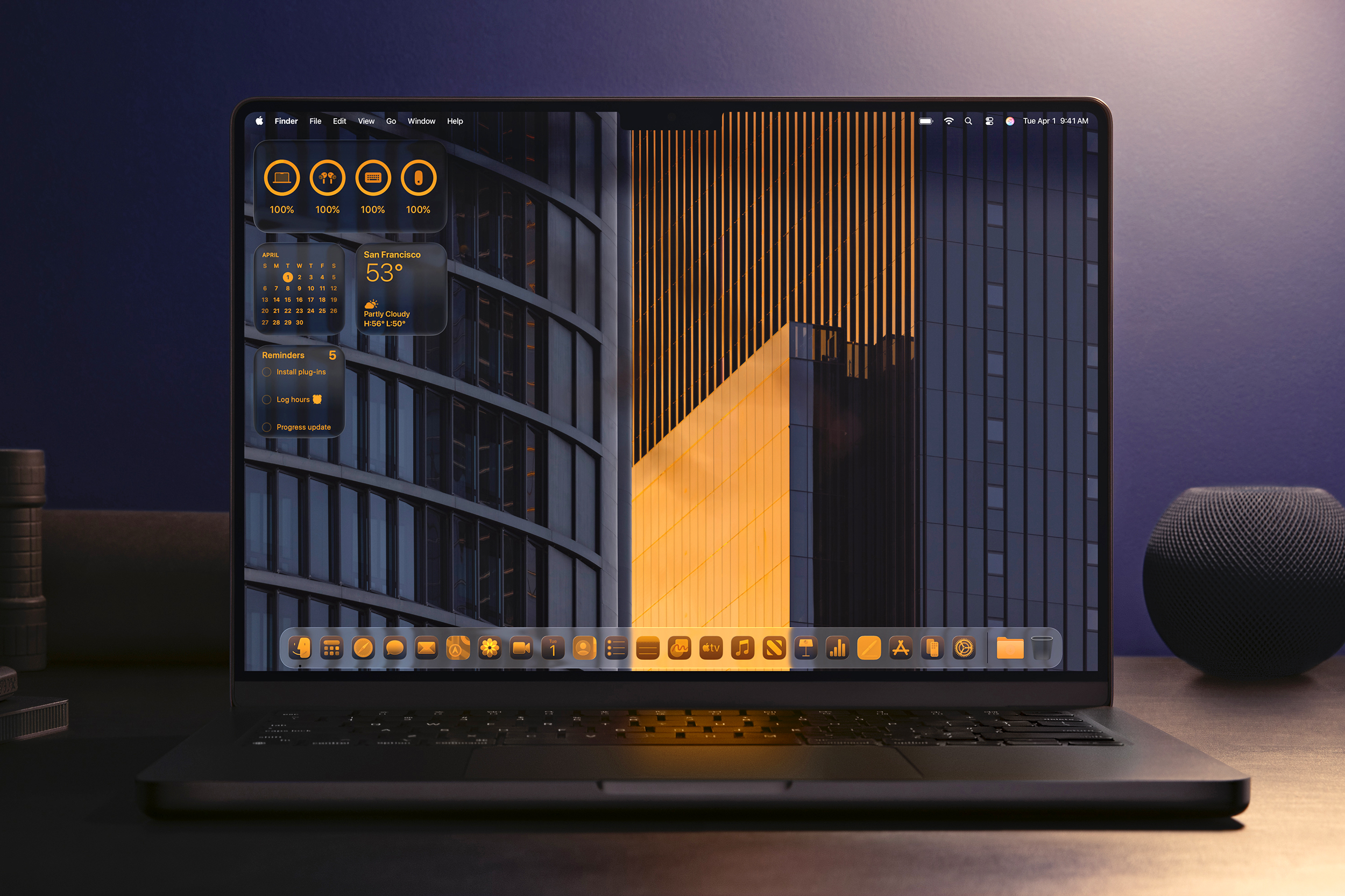 An Apple MacBook laptop running macOS Tahoe 26 on a desk next to Apple’s smart speakers.