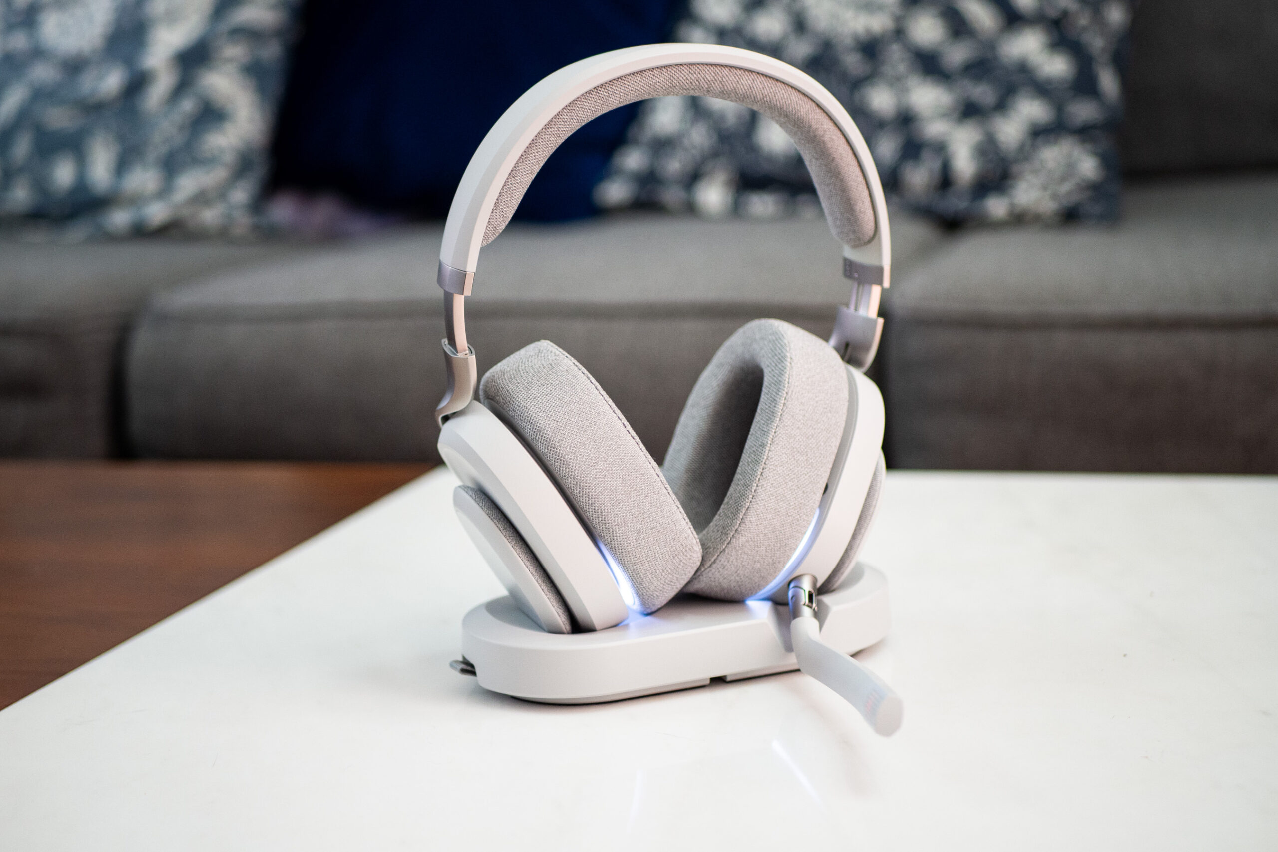 An image of the Fractal Scape gaming headset in gray resting on its charging dock. Its RGB LEDs are glowing subtly. The dock is positioned on a table surface that looks like marble.