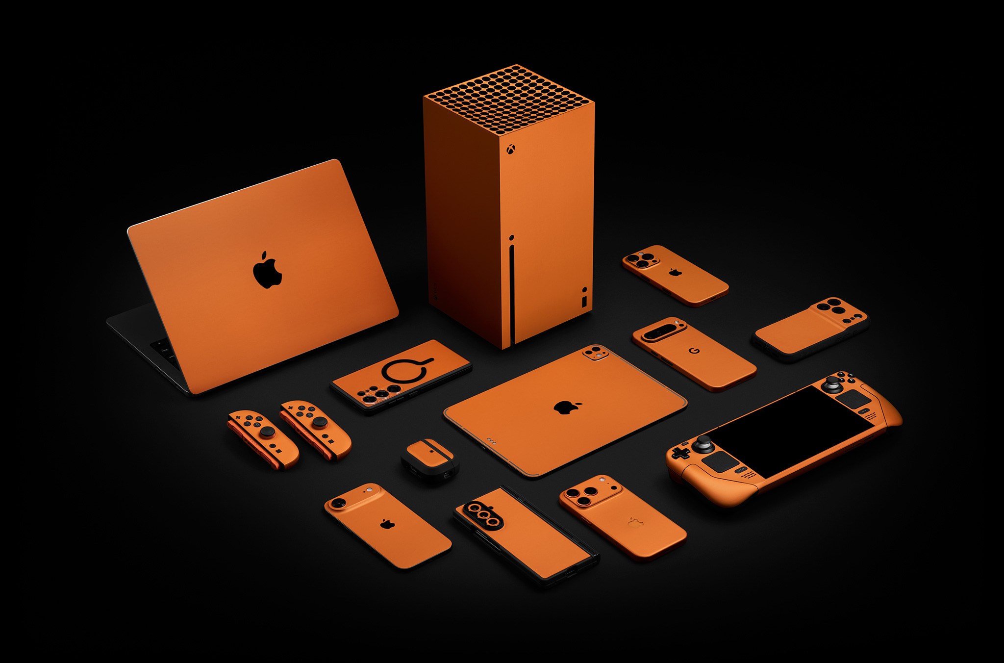 A selection of smartphones, laptops, tablets, and gaming hardware in Dbrand’s iPhone 17 Pro-inspired orange skins.
