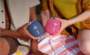 Two people holding UE WonderBoom 4 speakers, one blue and one pink.