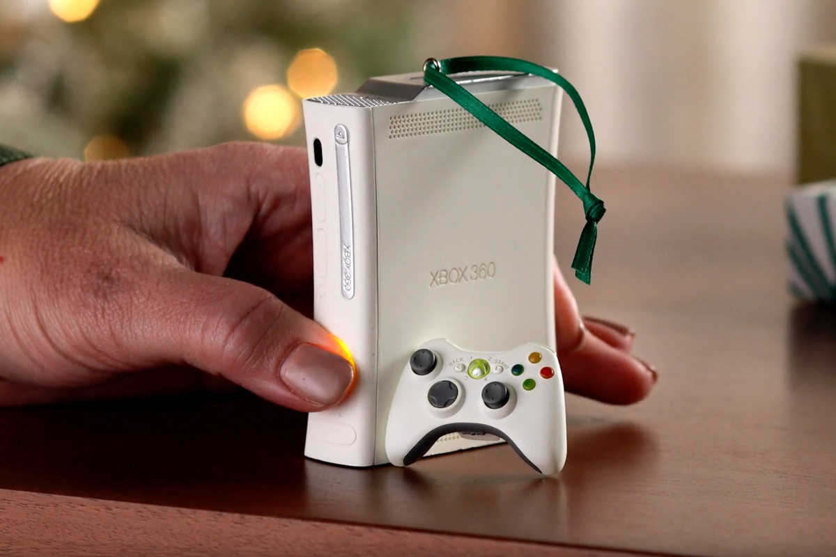 A person presses the power button on the Hallmark Xbox 360 Keepsake ornament sitting on a wooden table.