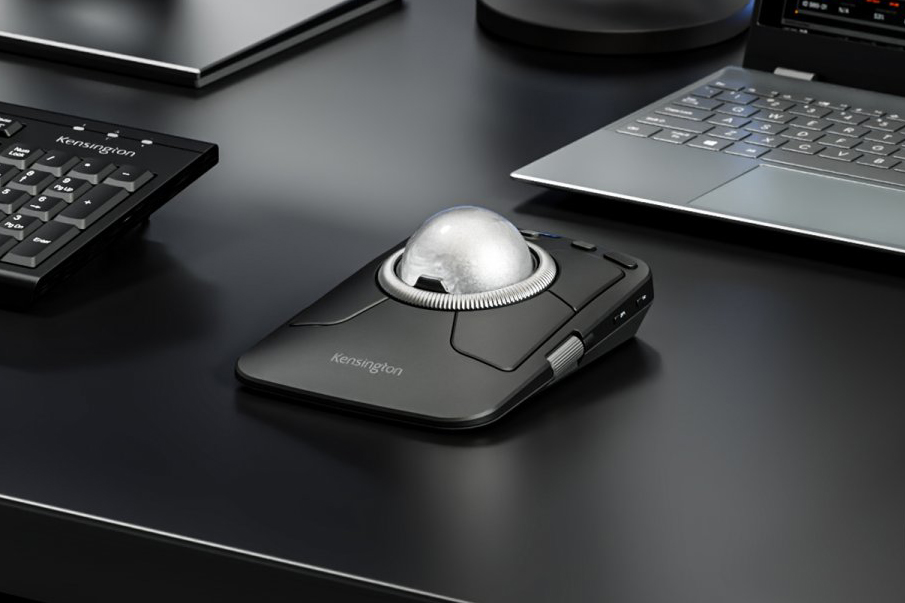 Kensington’s new Expert Mouse trackball on a black desk surrounded by keyboards and laptops.