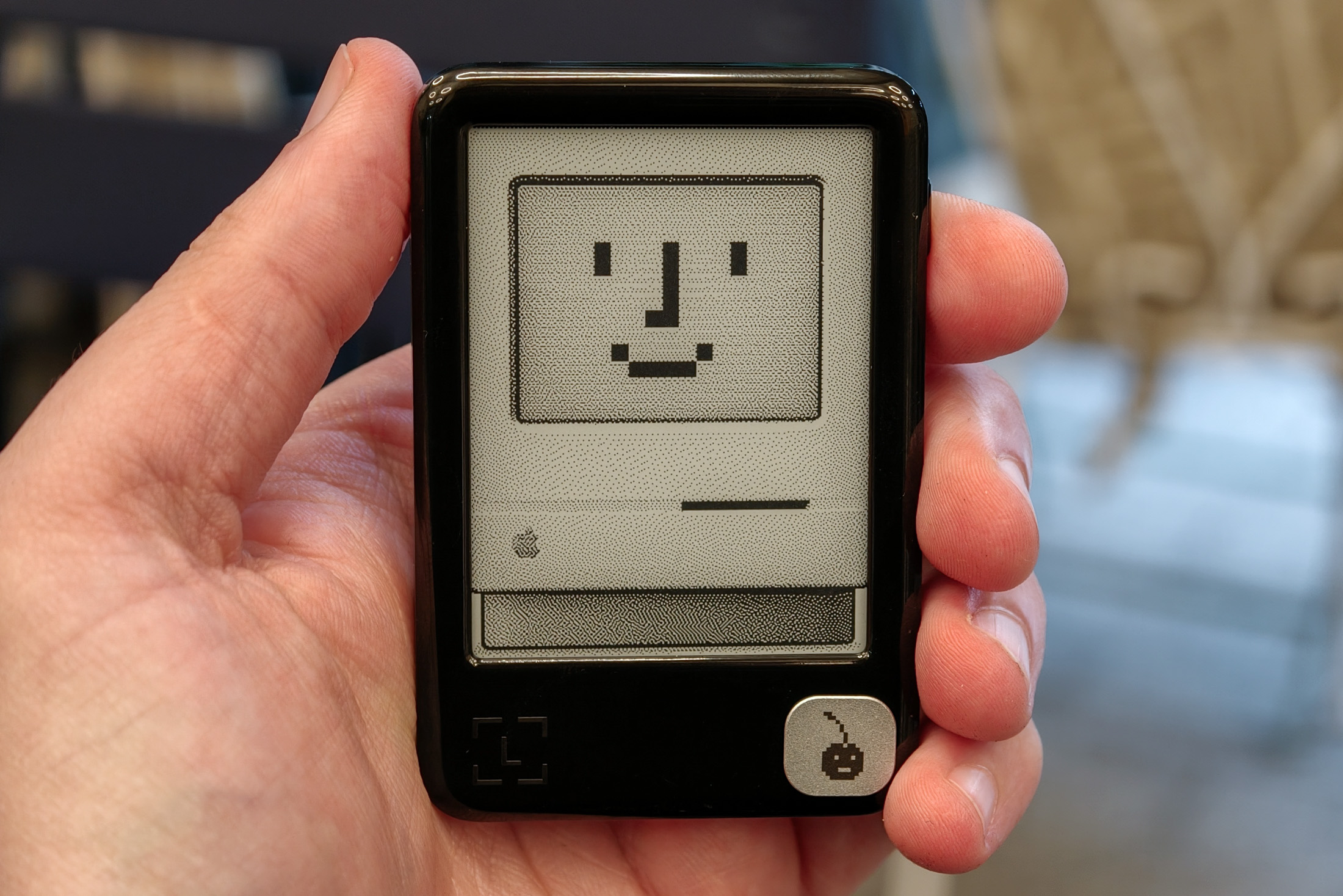 A photo of the Ledger Nano Gen5 held in a hand with a Mac wallpaper