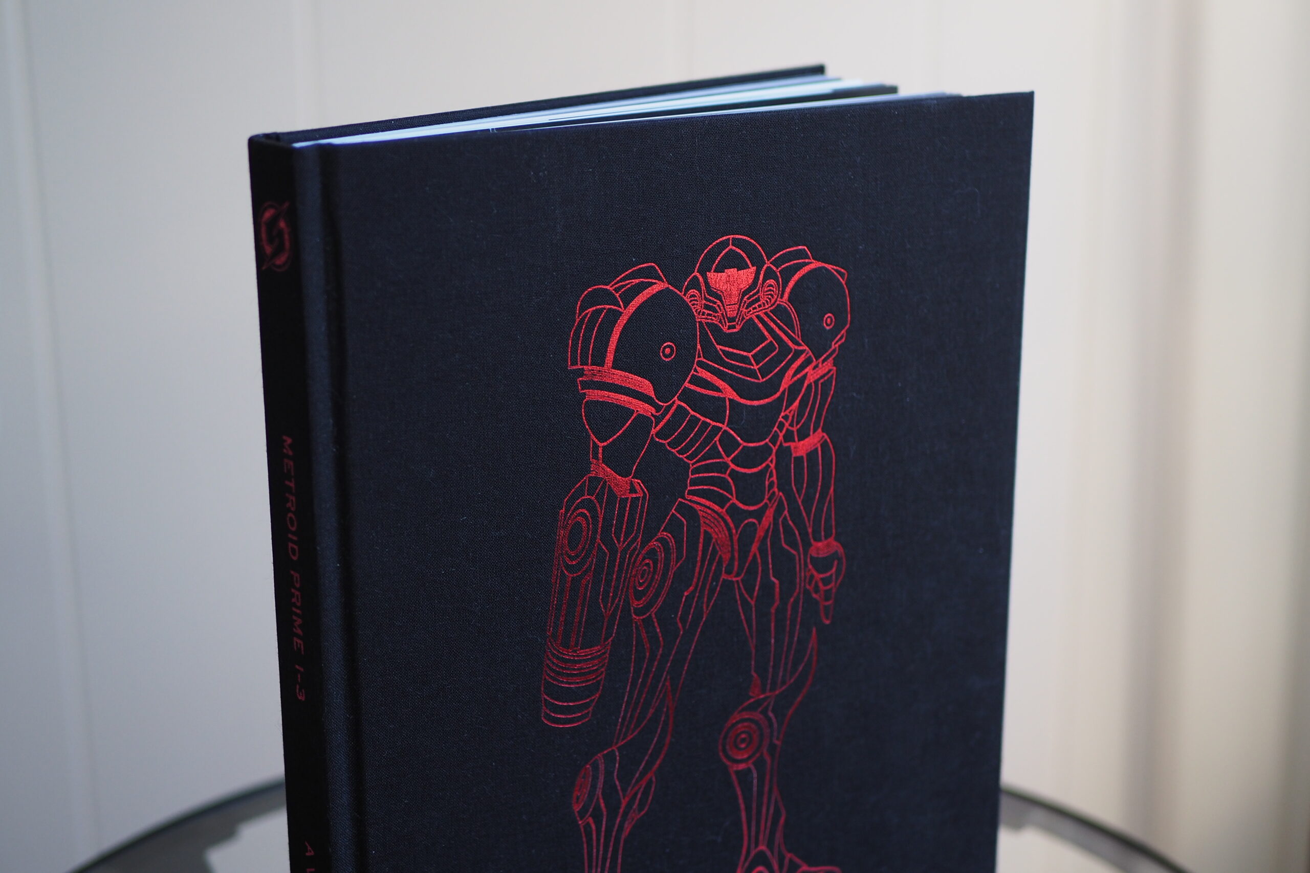 An image showing the black cover of the Metroid Prime 1-3 Visual Retrospective art book, which features Samus embossed in red.