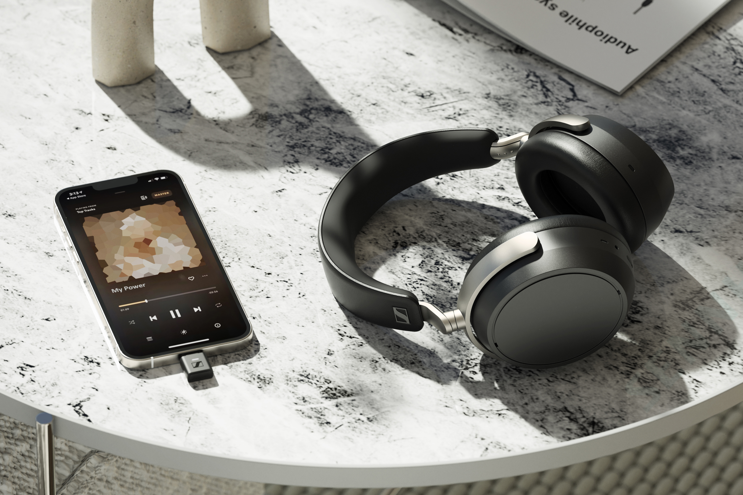 The Sennheiser HDB 630 headphones on a table next to a smartphone playing music with a dongle attached.