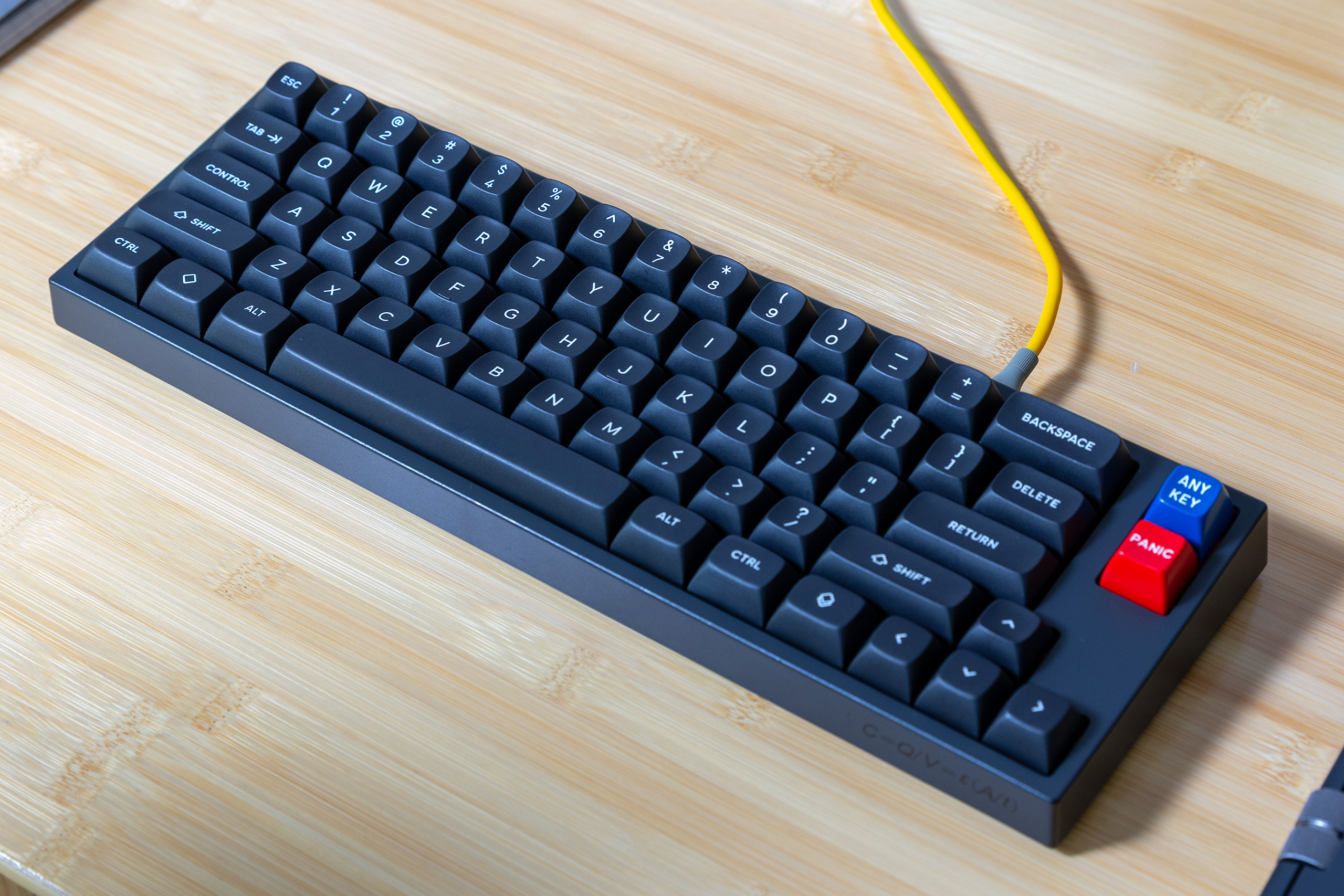 A black compact keyboard with white-on-black keycaps, on a bamboo desk. 