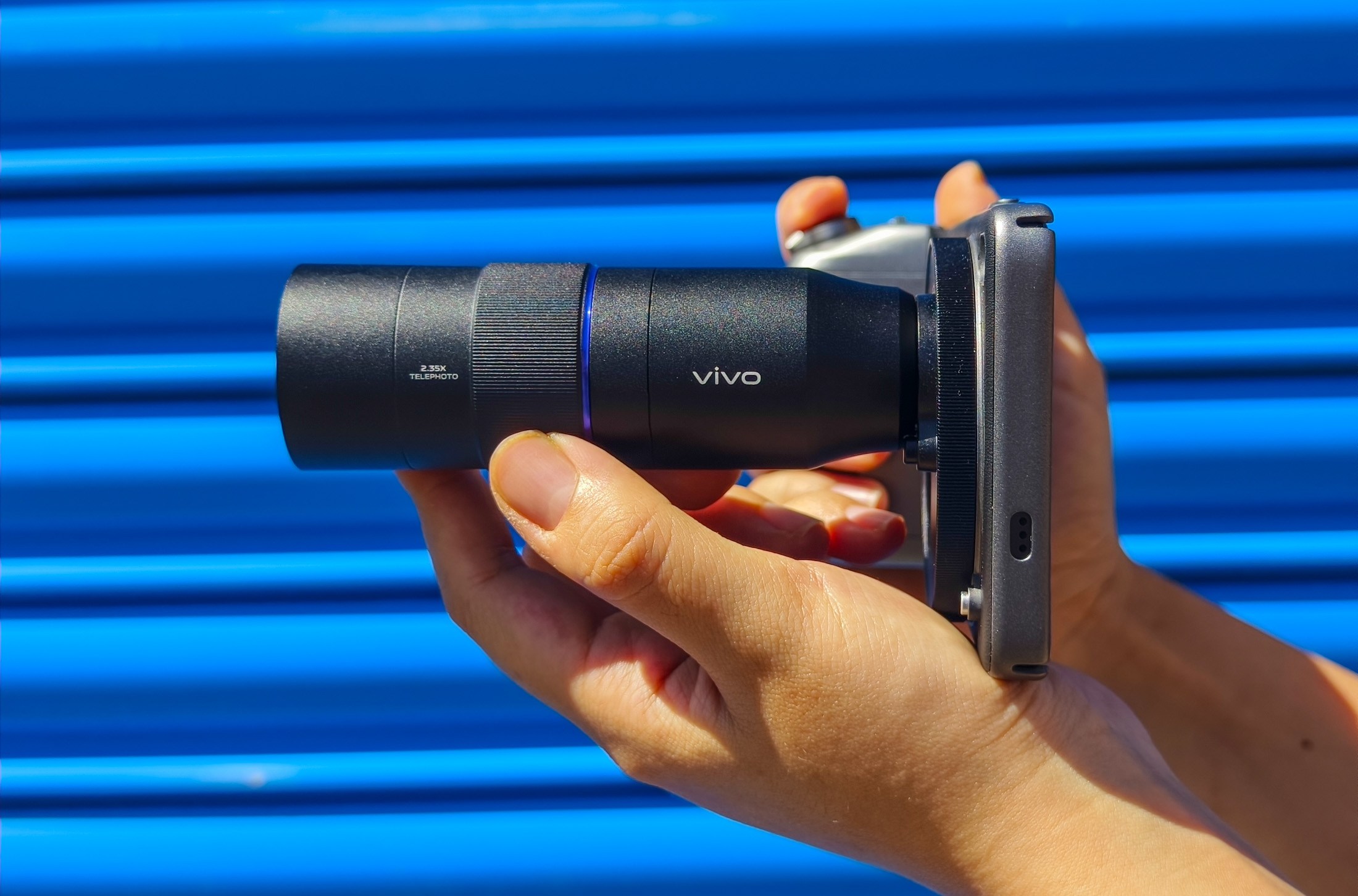 Vivo X200 Ultra with telephoto extender lens attached, in front of a blue metal gate.