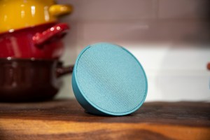 Teal Amazon Echo Pop viewed at an angle with colorful pots in the background.