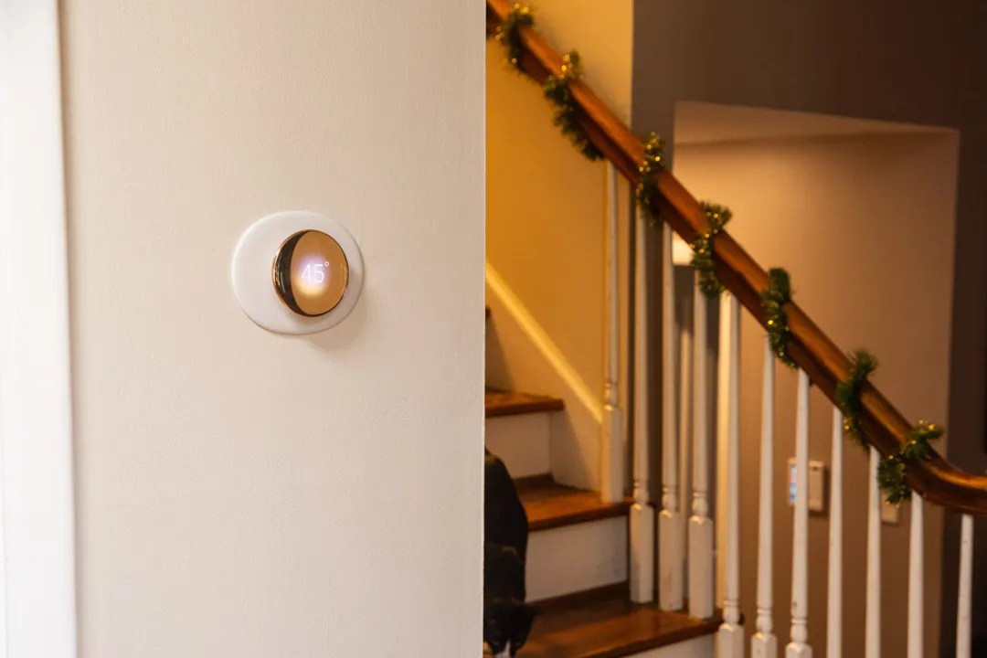 The fourth-gen Google Nest Learning Thermostat hung up on a wall near a staircase.
