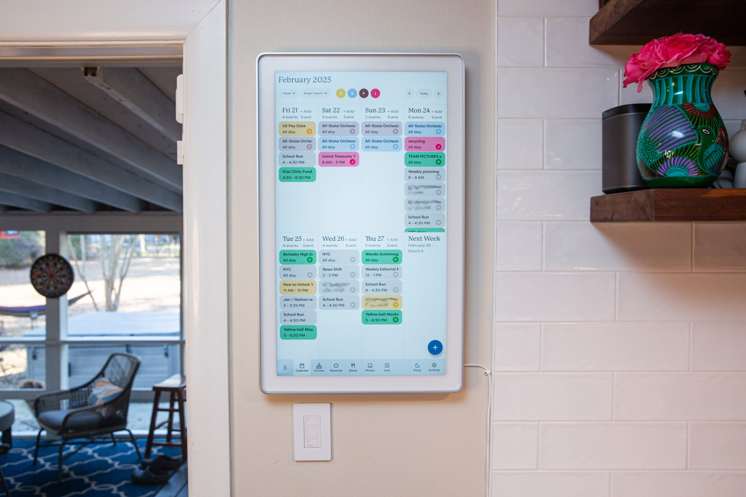 A 27-inch touchscreen digital calendar mounted on a wall in a kitchen.