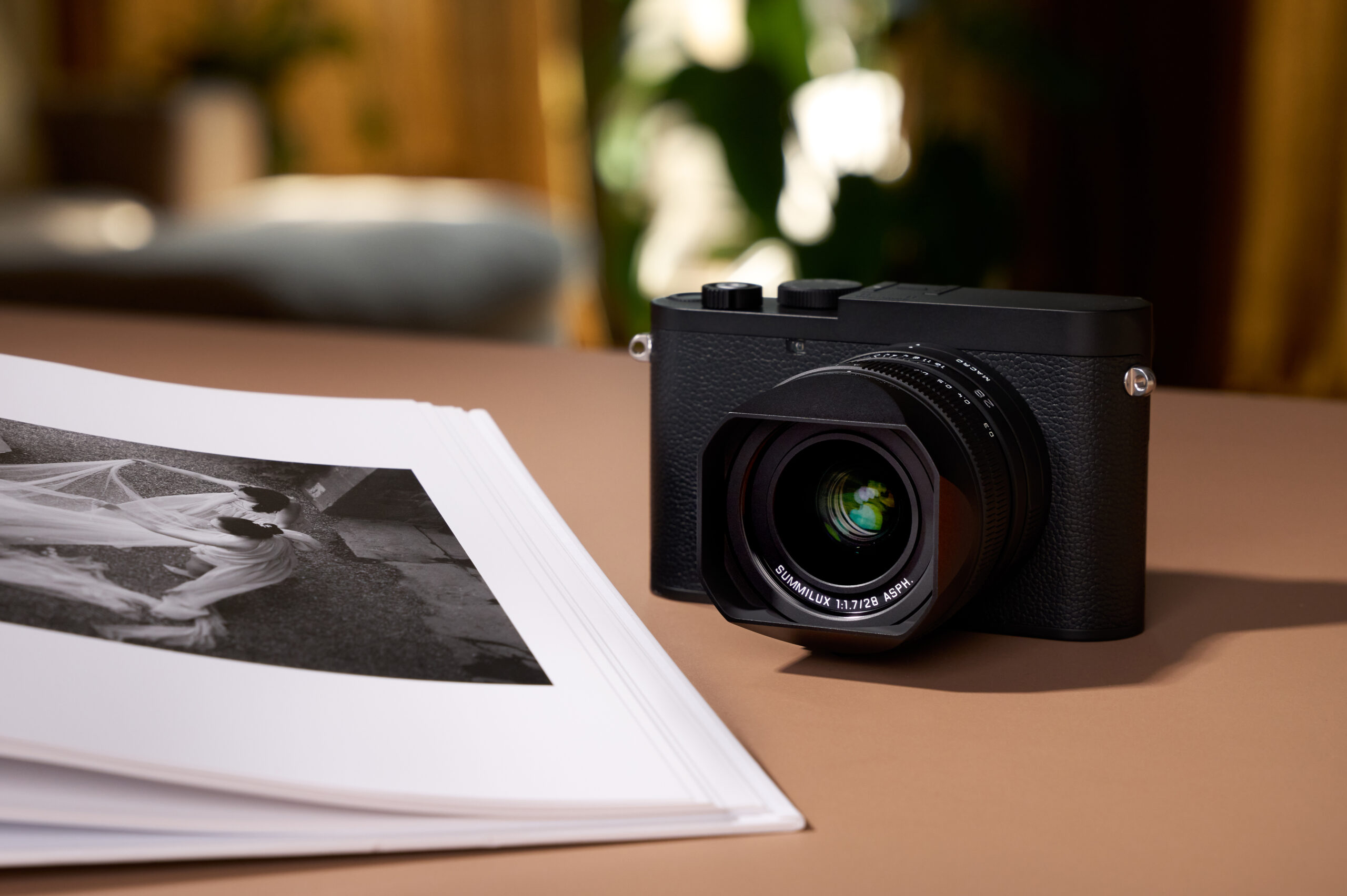 A Leica Q3 Monochrom camera on a table, beside an open art book displaying a black-and-white photo.