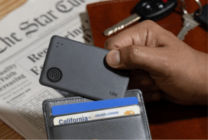 A hand placing a Tile Slim into a leather wallet with a newspaper in the background.