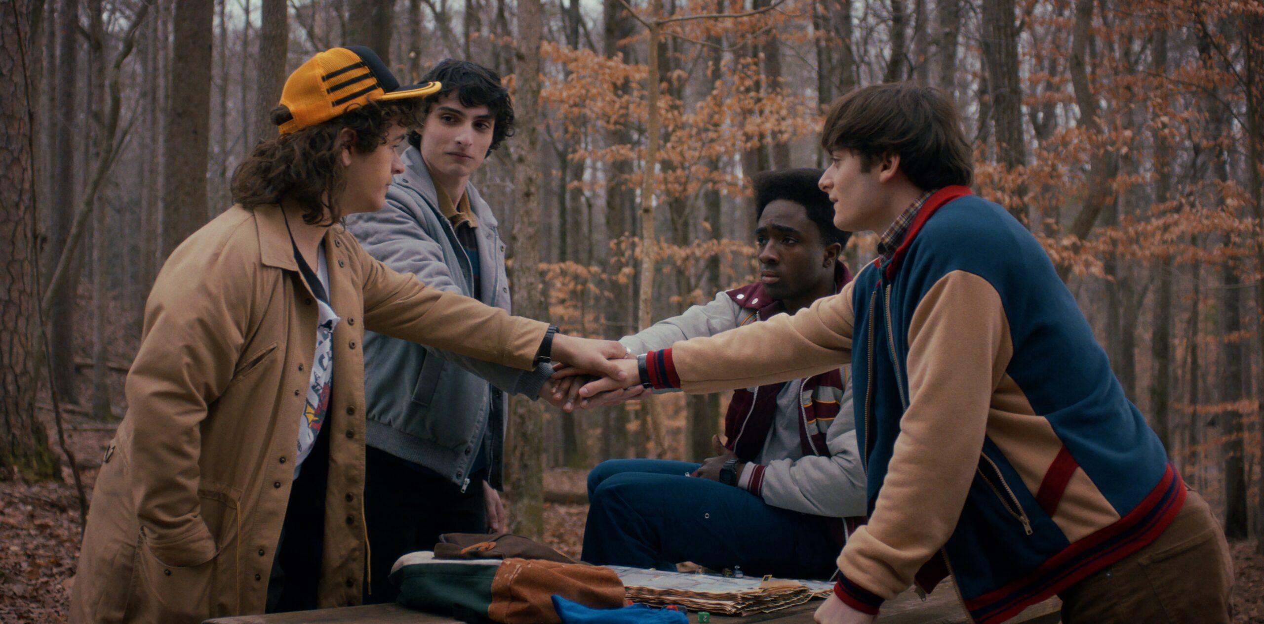 Four teenage boys standing together in the woods while putting their hands together.