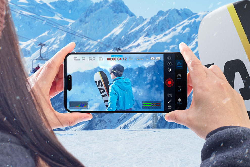 A person records a snowboarder using the Blackmagic Camera app on a smartphone.