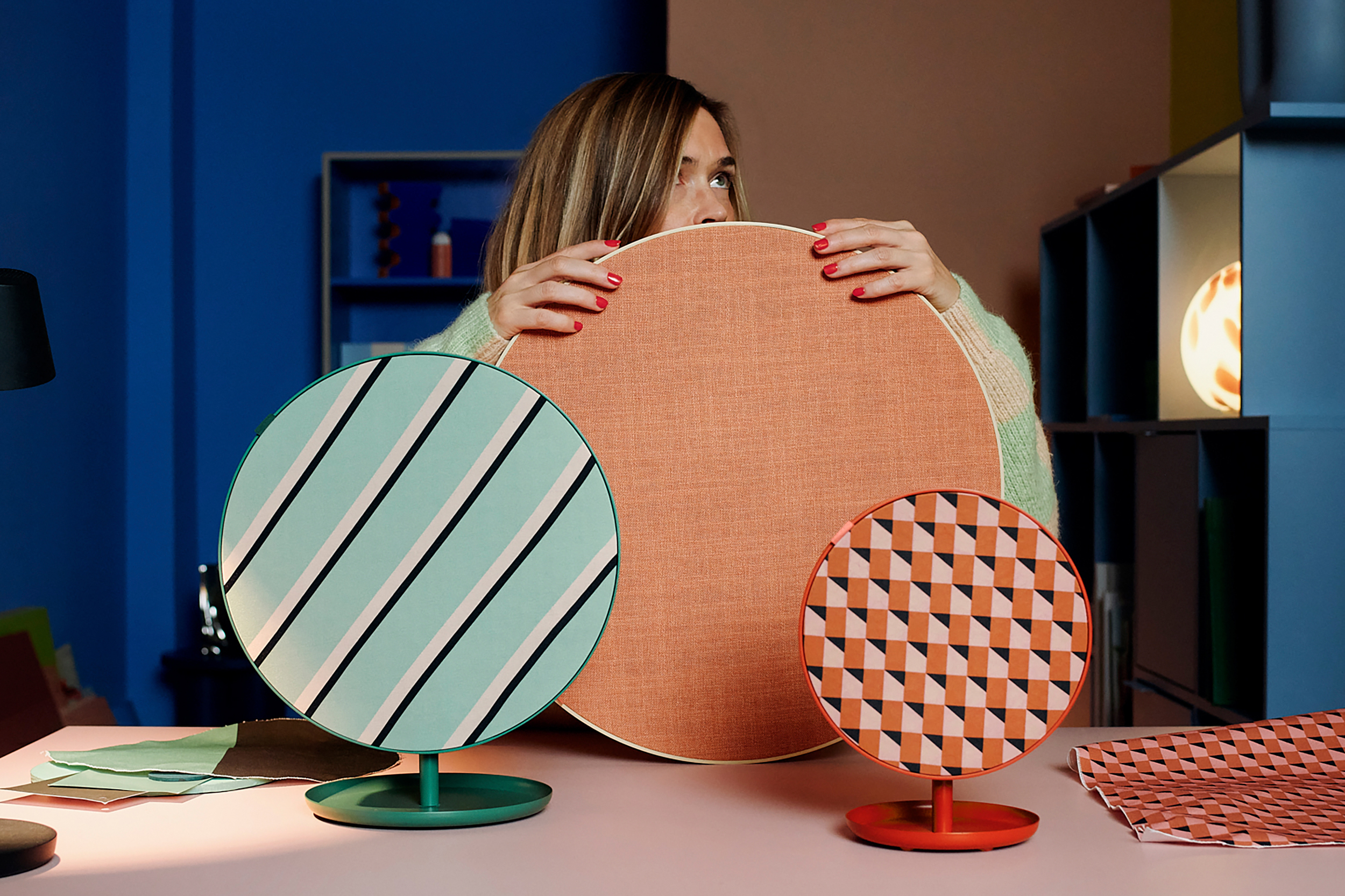 Three Ikea Bluetooth speakers on a table with the largest being held up by a designer.