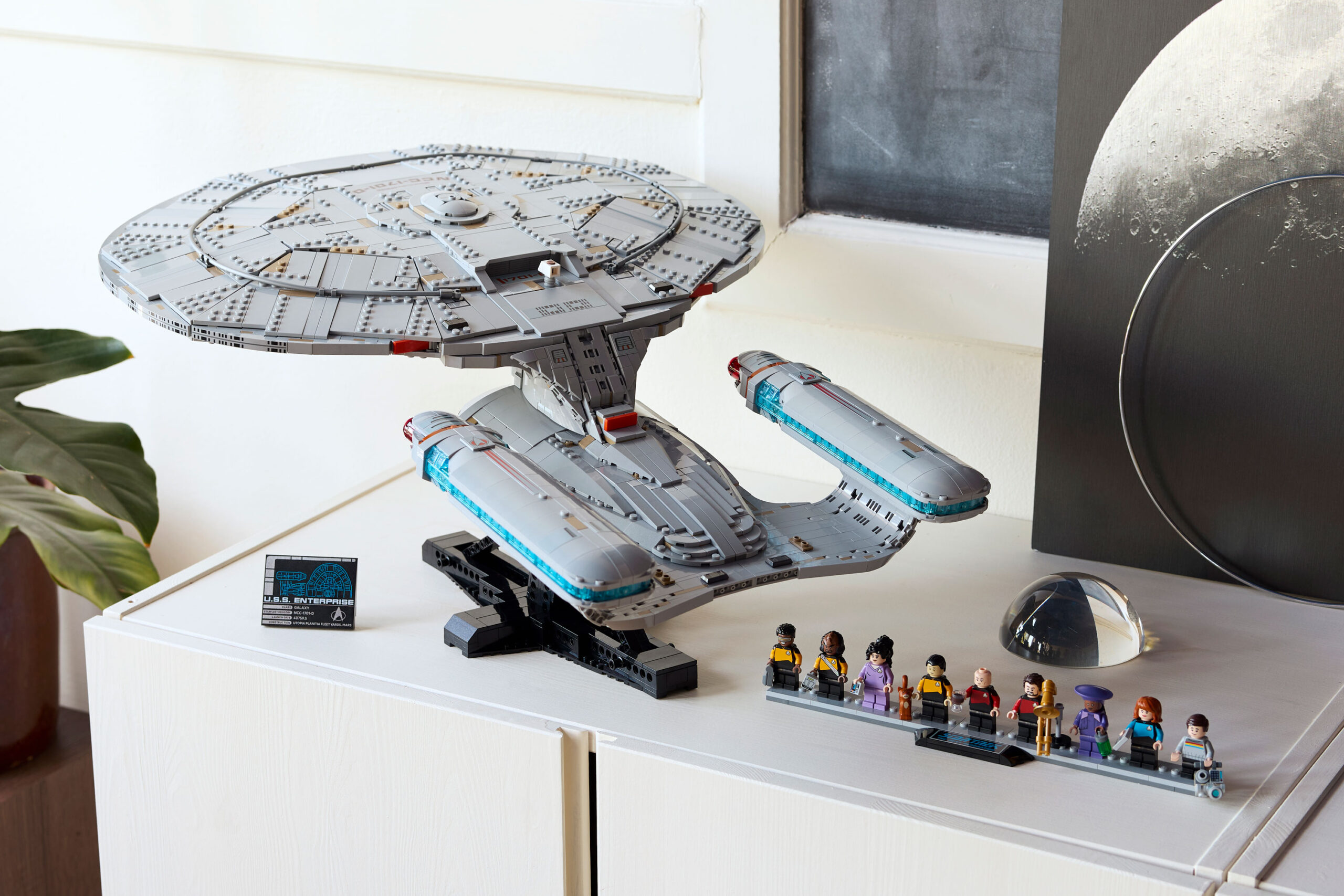 Lego’s Star Trek Enterprise replica on a white cabinet next to the nine included minifigures.