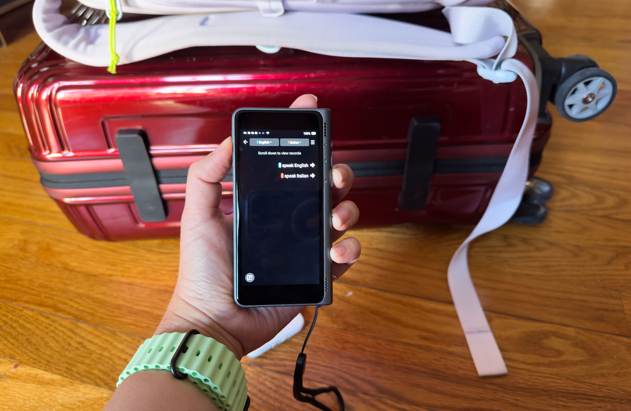 Top-down view of someone holding a TimeKettle T1 set to English and Italian with a suitcase in the background.