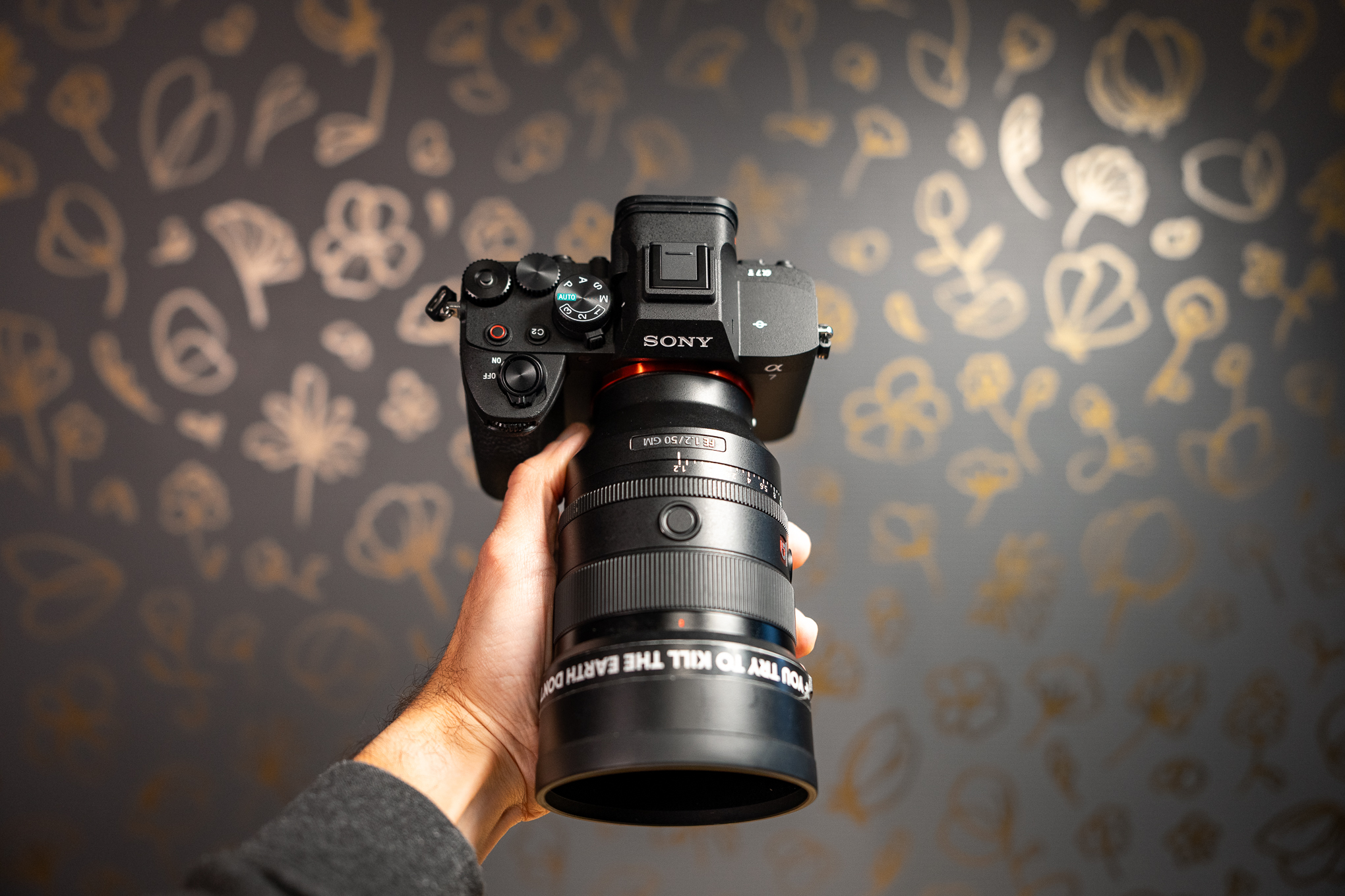 An outstretched hand holding a Sony A7 V camera by its lens.