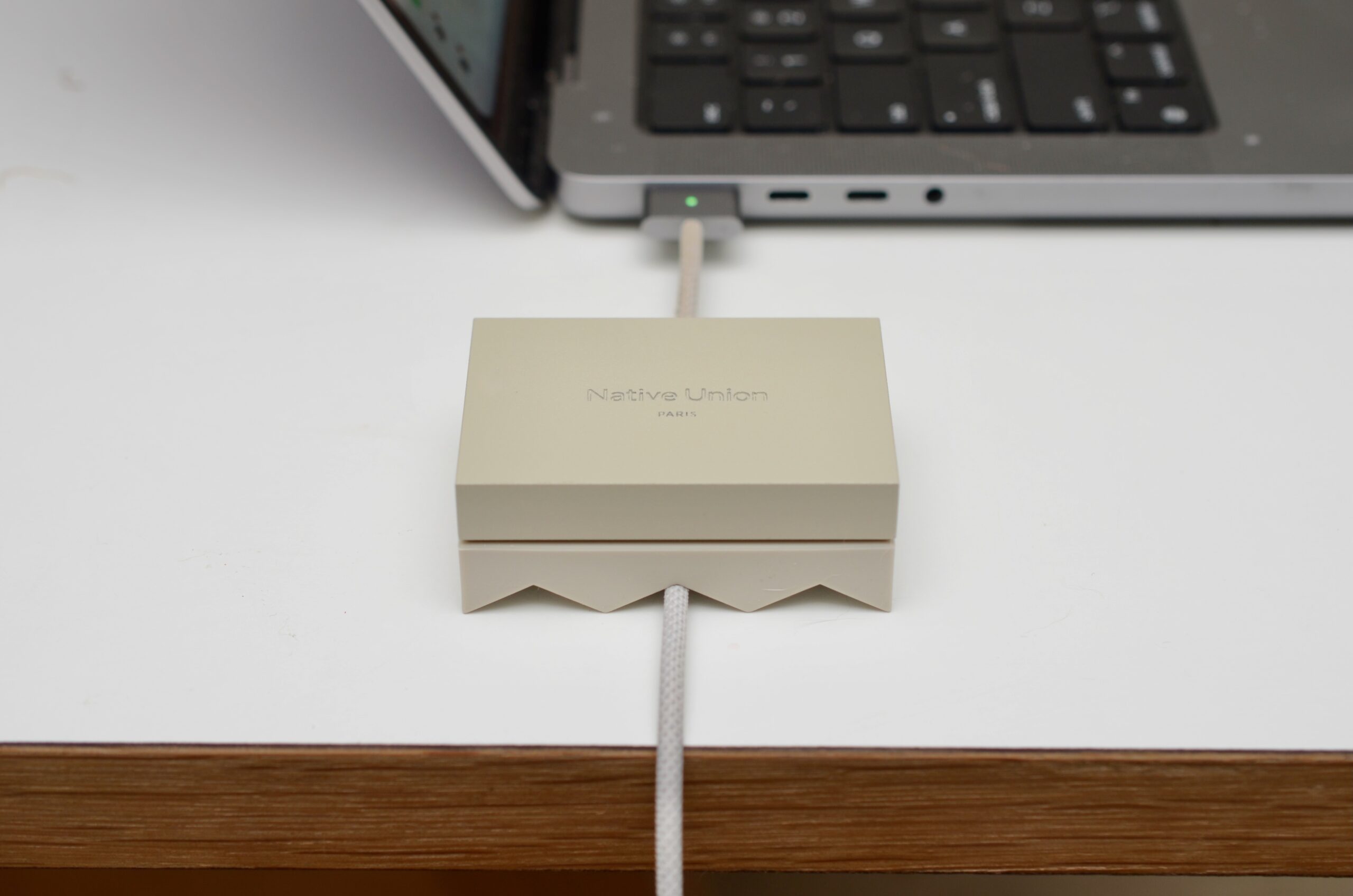Native Union’s Weighter sits on a table with an Apple charging cable snaking through one of three slots to a MacBook Pro charging in the background.