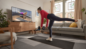Person stretching in front of TV streaming Peloton subscription content.