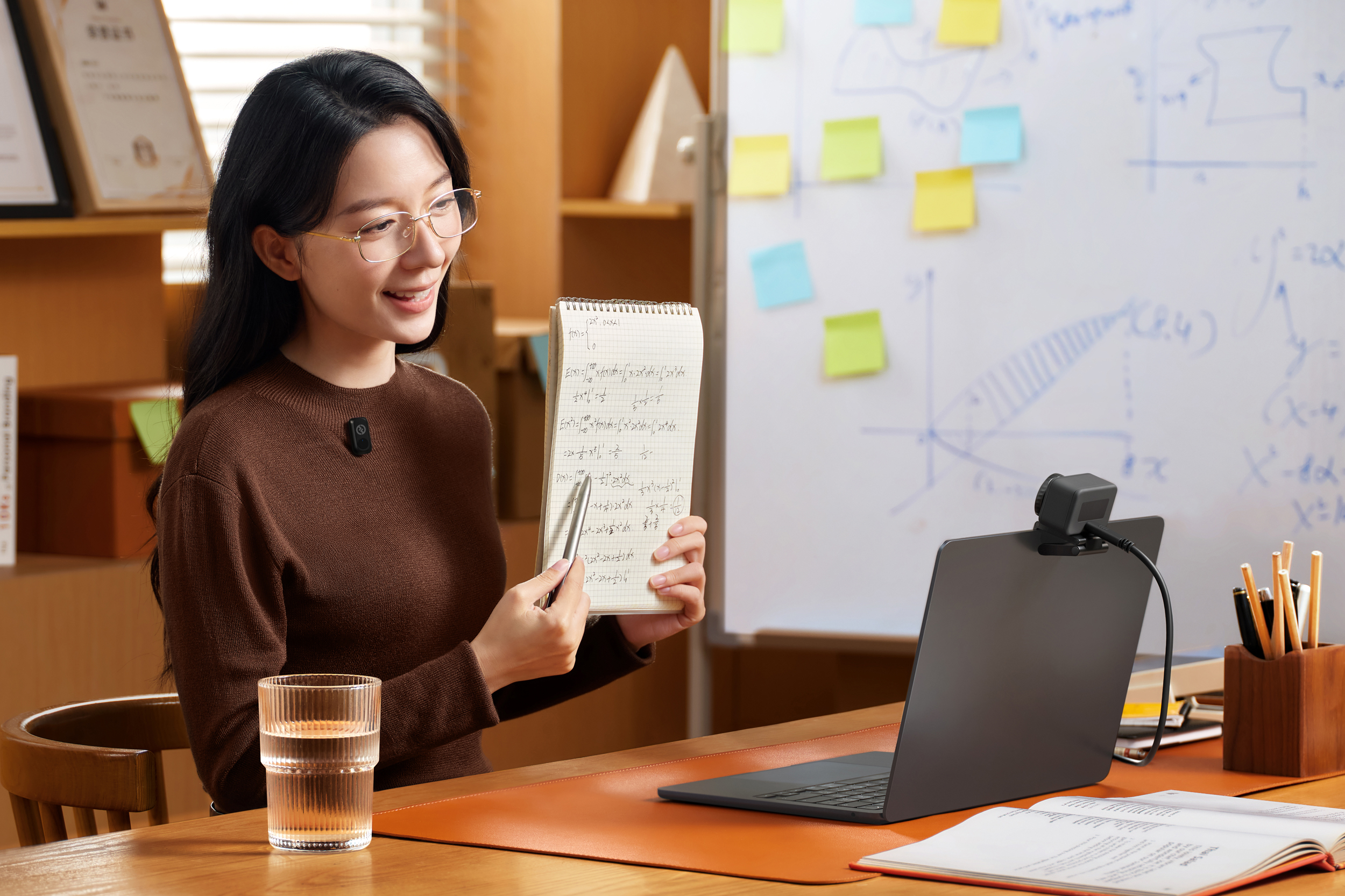 A person holds up a notebook to the Lyra webcam on a laptop while wearing a wireless lav mic.