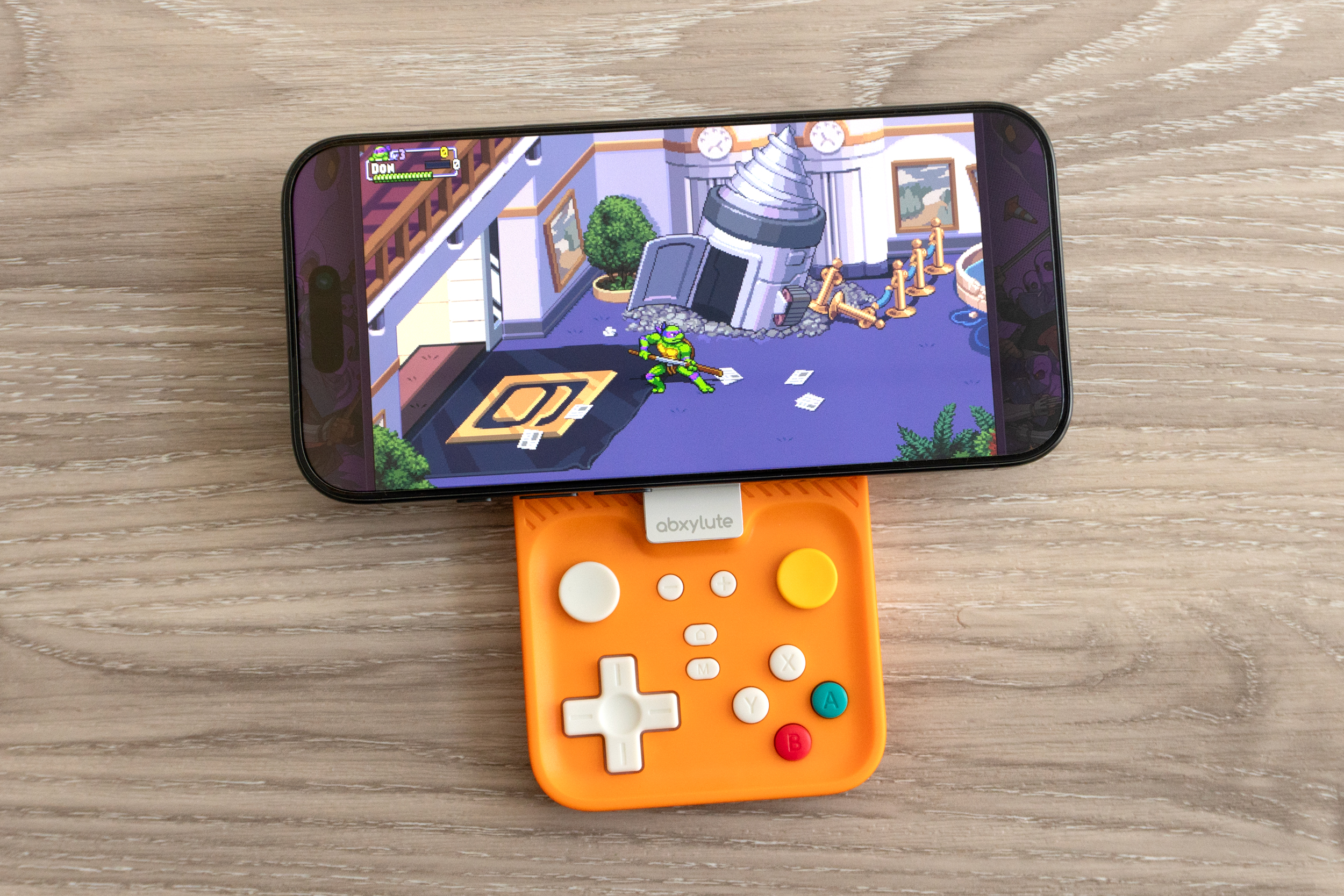An iPhone 16 Pro playing a TMNT game with the Abxylute M4 mobile controller attached.