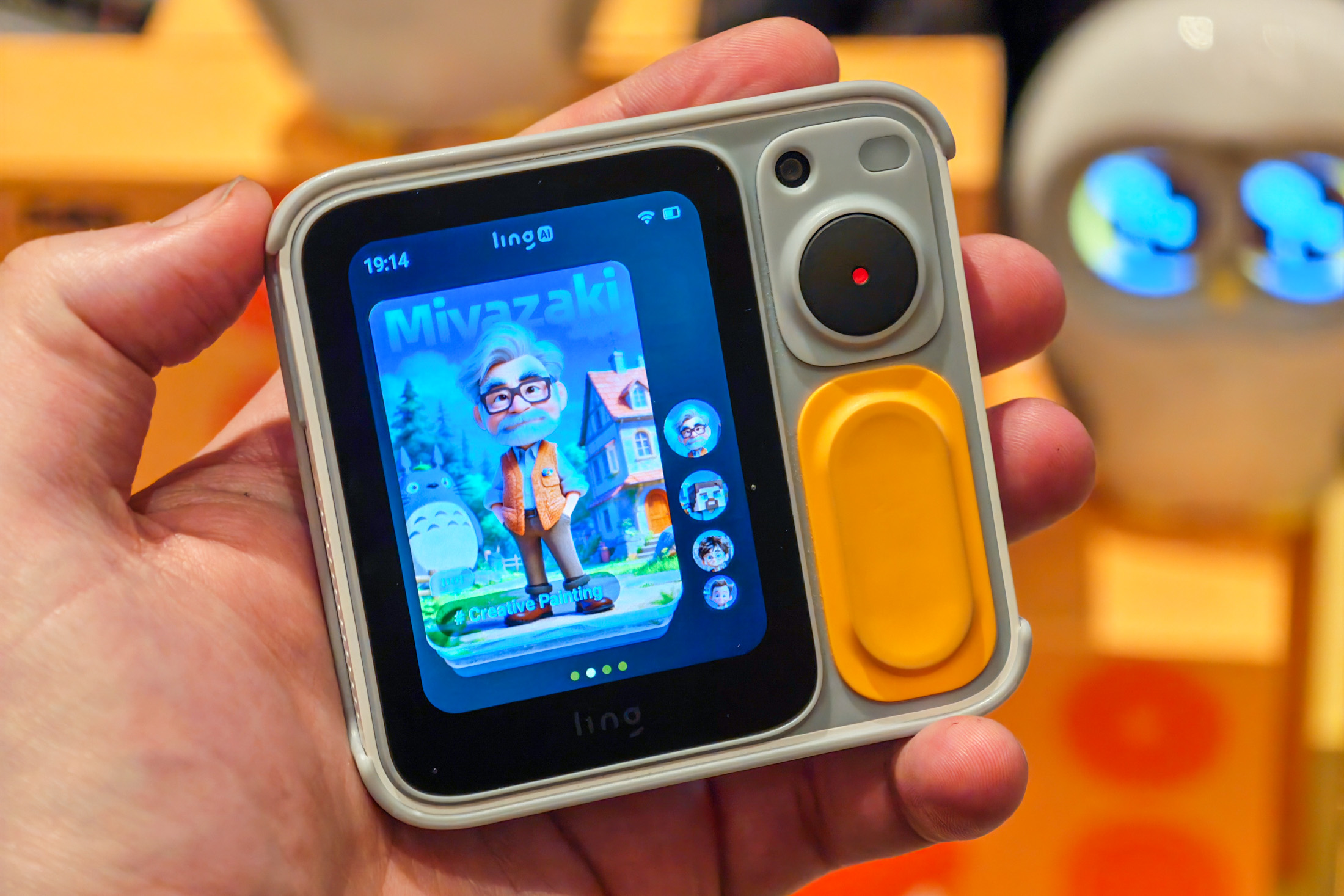 A palm-sized device with a small screen showing a cartoonish avatar of Studio Ghibli’s Miyazaki next to the character Totoro.