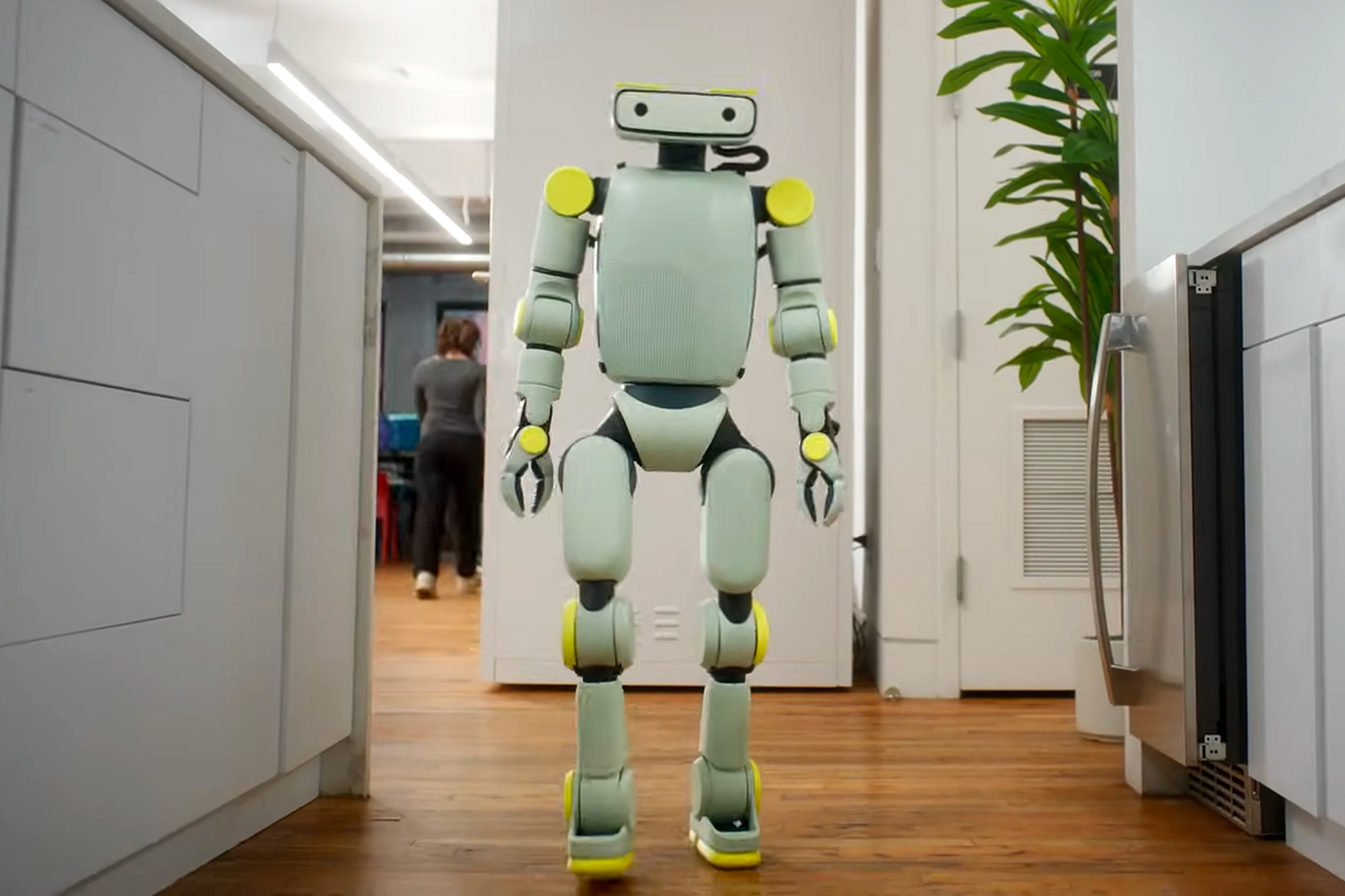 A humanoid robot walks down a hallway in an office setting.