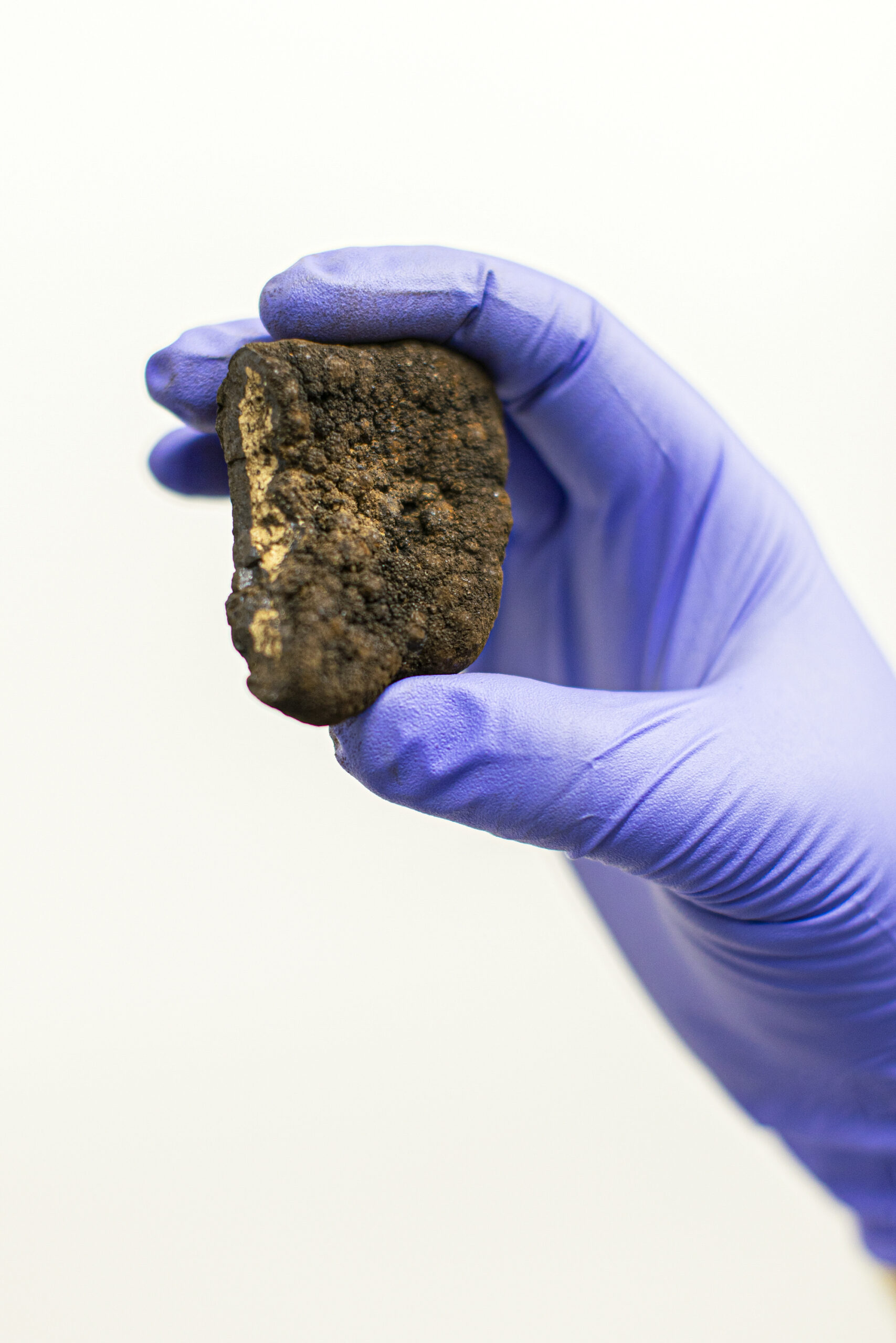 A gloved hand holds up a polymetallic nodule that looks like a dark rock.