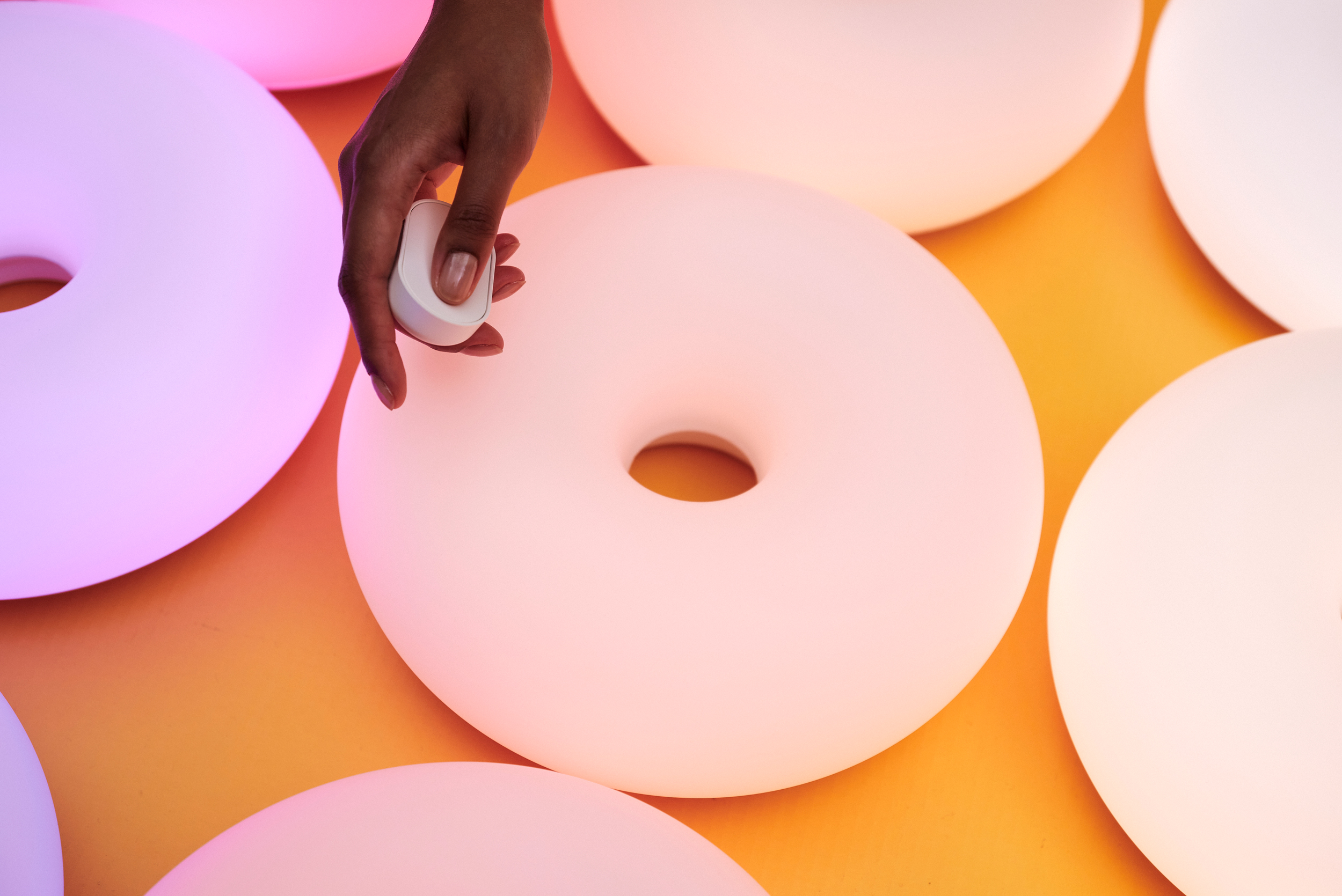 A person presses a button on a wireless remote near Ikea’s glowing Varmblixt smart donut lamp.