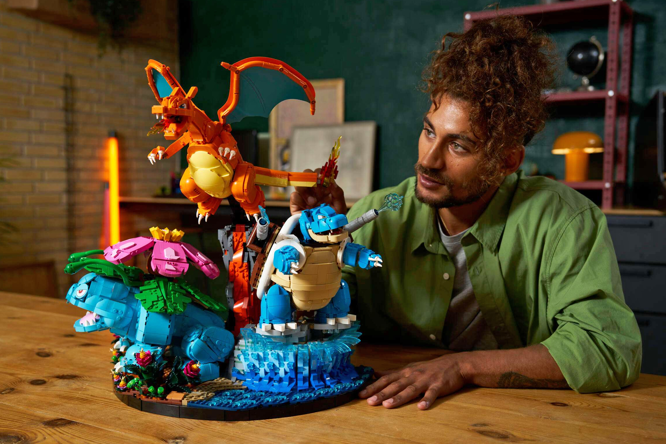 A person at a table next to Lego’s Venusaur, Charizard and Blastoise Pokémon building set.