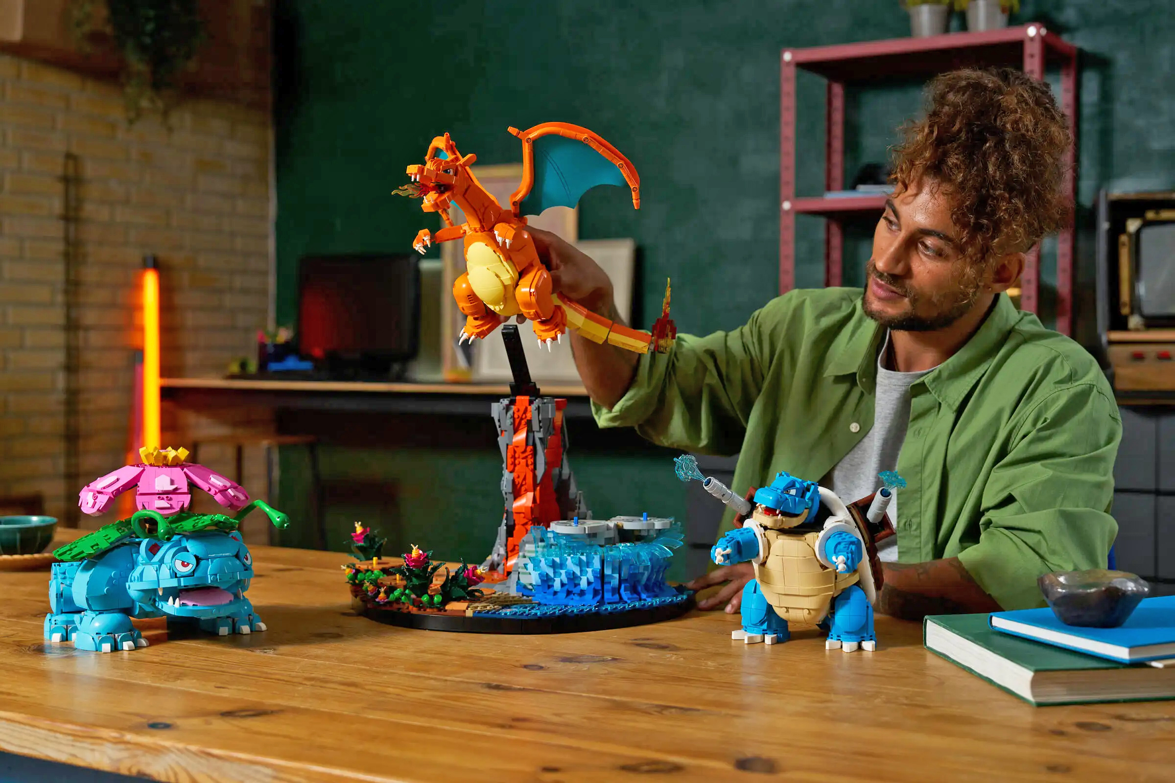 A person at a table next to Lego's Venusaur, Charizard and Blastoise Pok&eacute;mon building set.