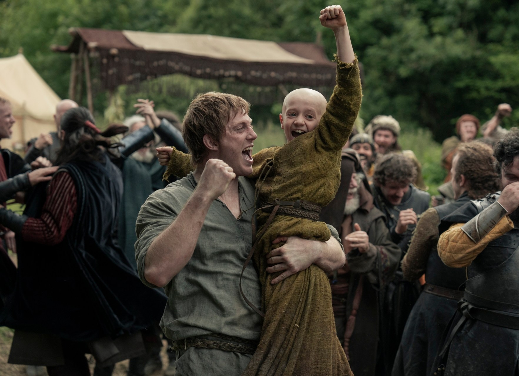 A cheering man holding a cheering boy. The pair are surrounded by a group of cheering men.