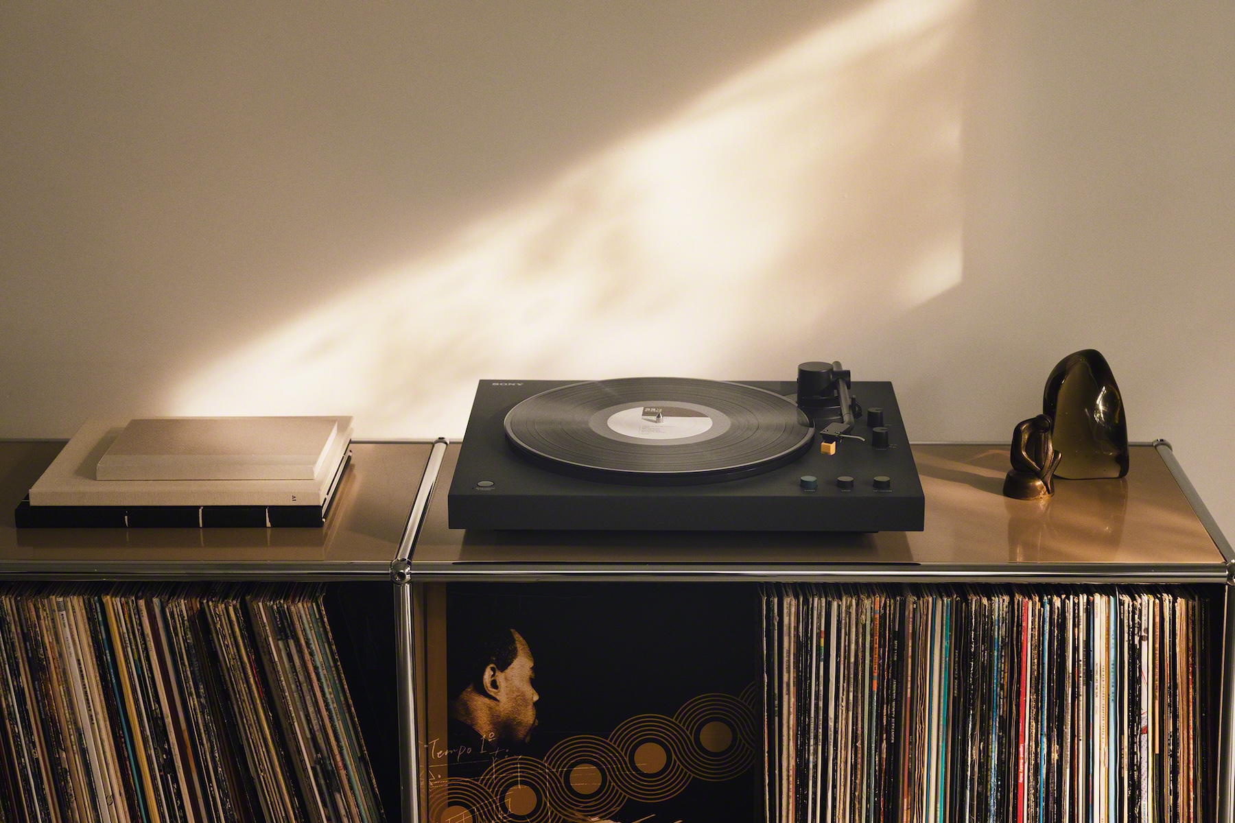 The Sony PS-LX5BT turntable next to decorative art on a stand that’s holding records.