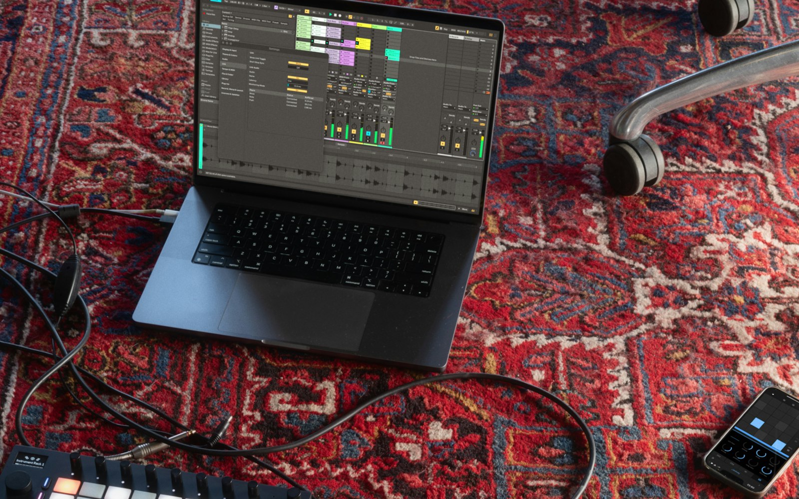 A laptop on a floor running Ableton Live 12.4 beta with an iPhone running Ableton Not on one side and an Ableton Move just poking into the bottom of the frame.