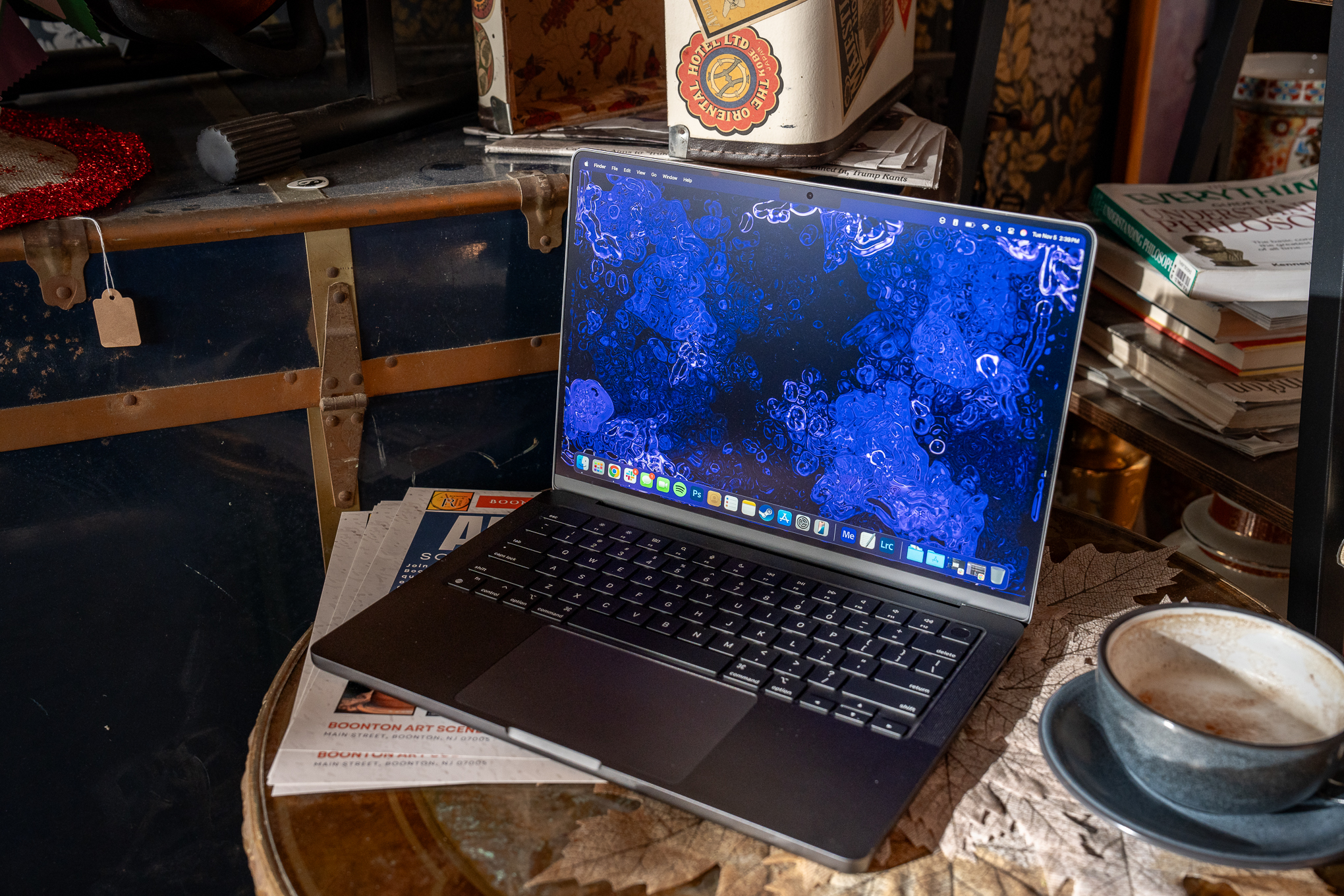 A 14-inch MacBook Pro M4 (2024) in space black sitting on an end table at a cafe with a coffee beside it.