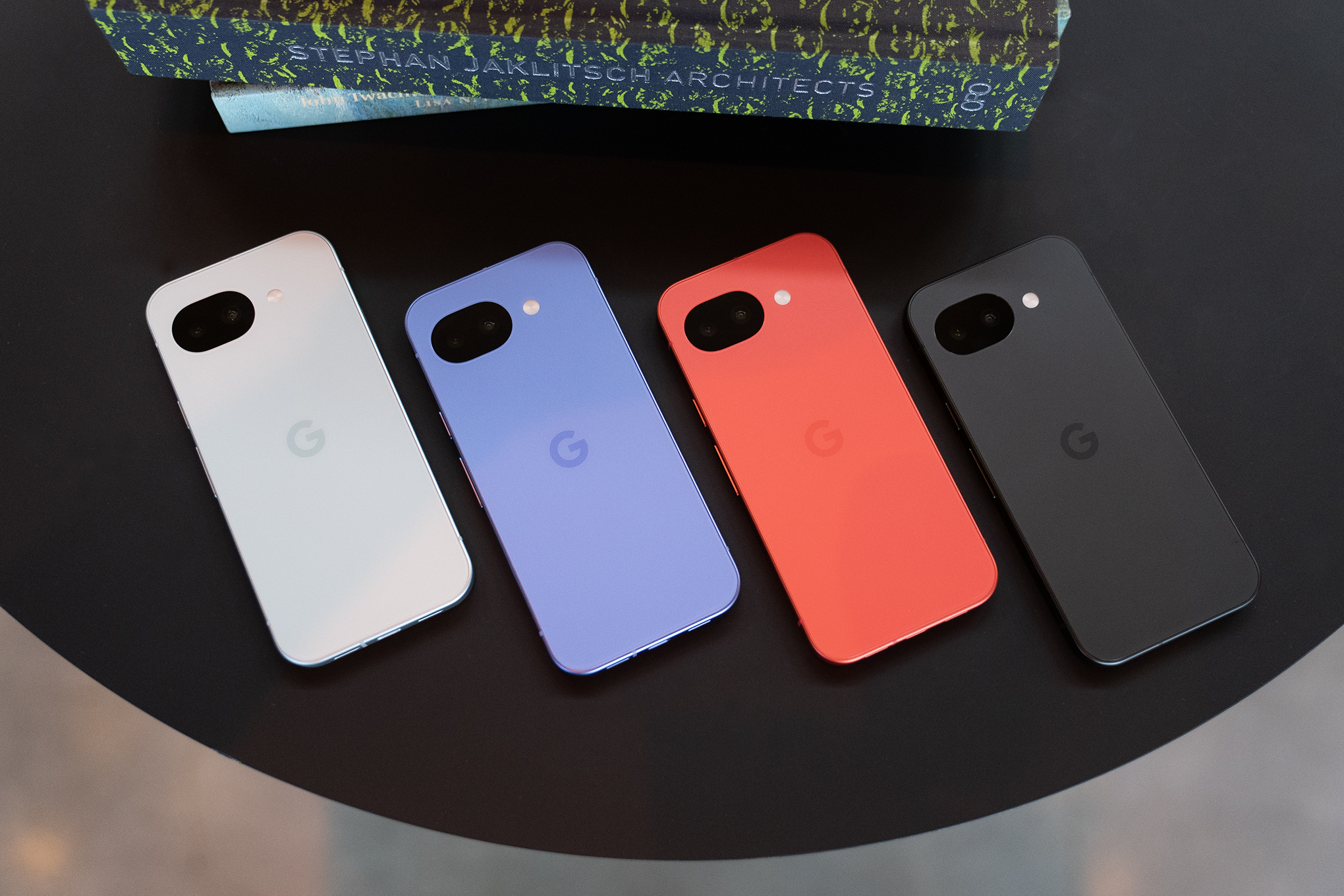 Four Google Pixel 10As in a variety of colors on a black tabletop.