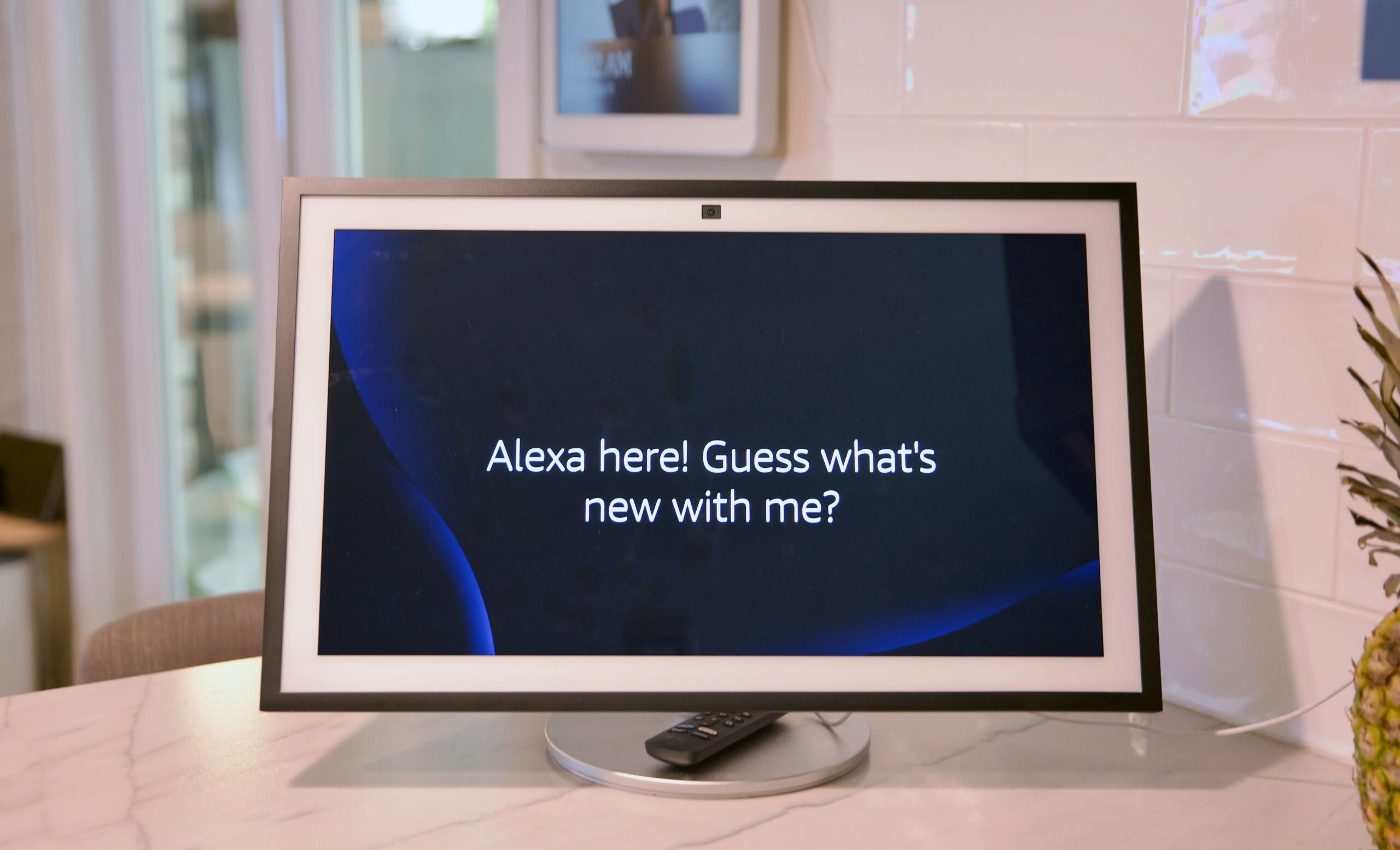 A large smart display on a kitchen counter displaying the words “Alexa here! Guess what’s new with me?”