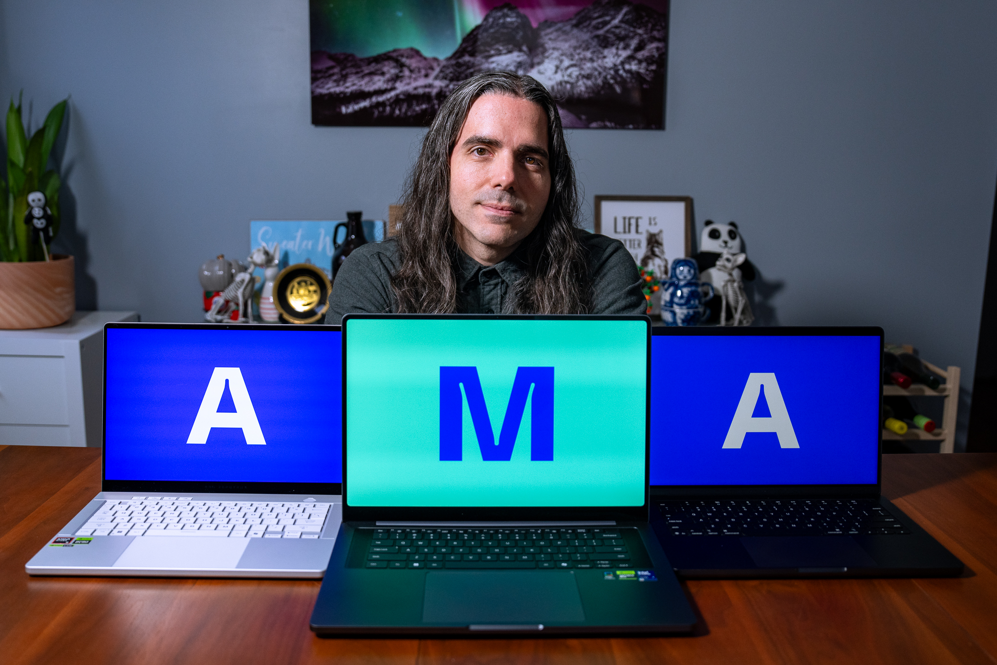 A person sitting at a table behind three laptops. Each laptop has a single letter displayed onscreen, spelling out A-M-A.